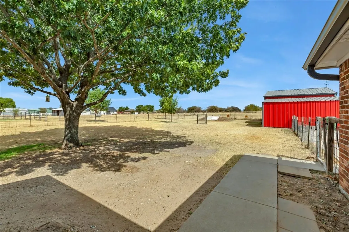 Expansive outdoor space featuring a mature tree, concrete patio, and a red metal barn structure with a gray roof
