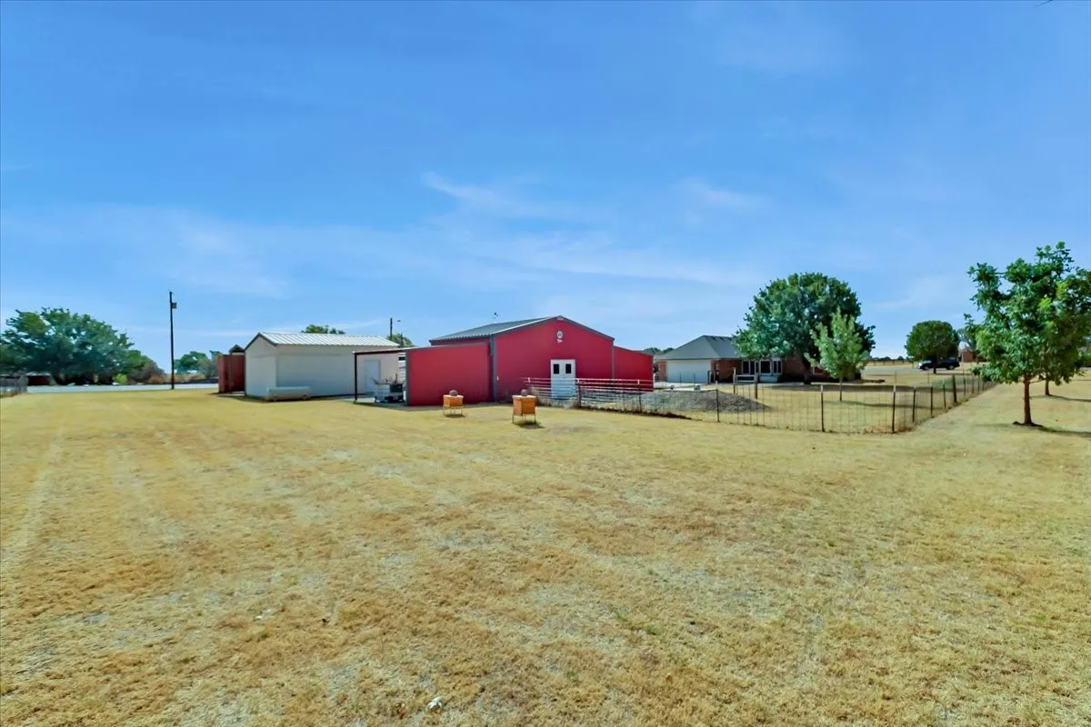 Expansive property with a red barn structure, white auxiliary building, and chain link fencing