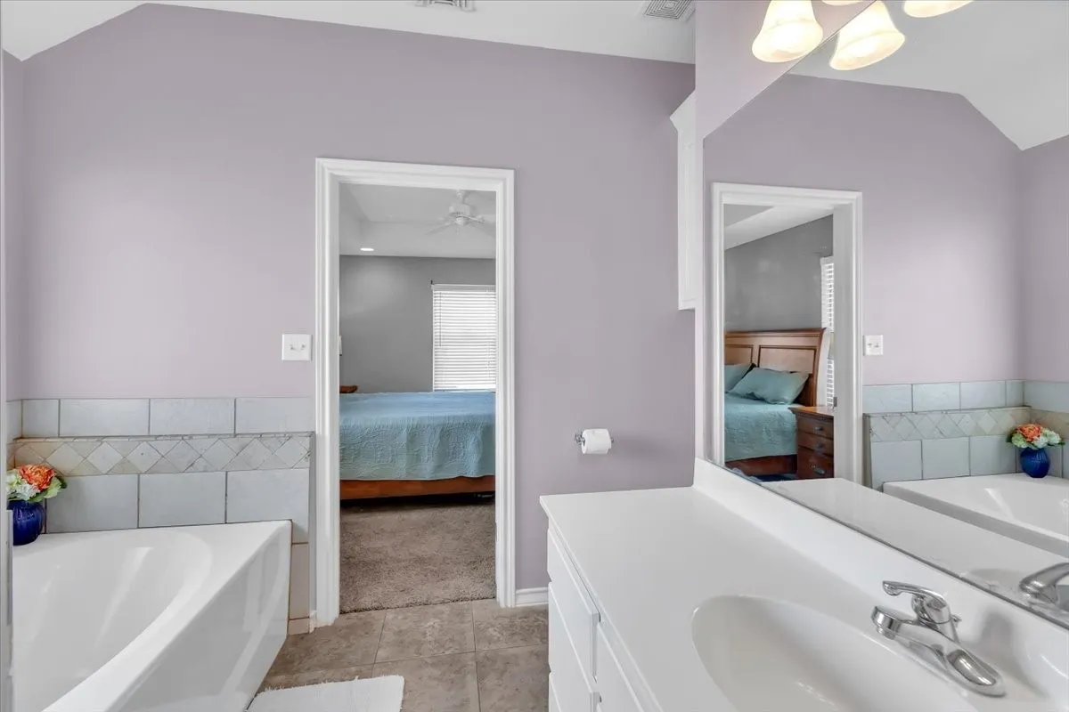 Bathroom featuring a built-in bathtub, tile surround, vanity with an integrated sink, and wall-mounted lighting