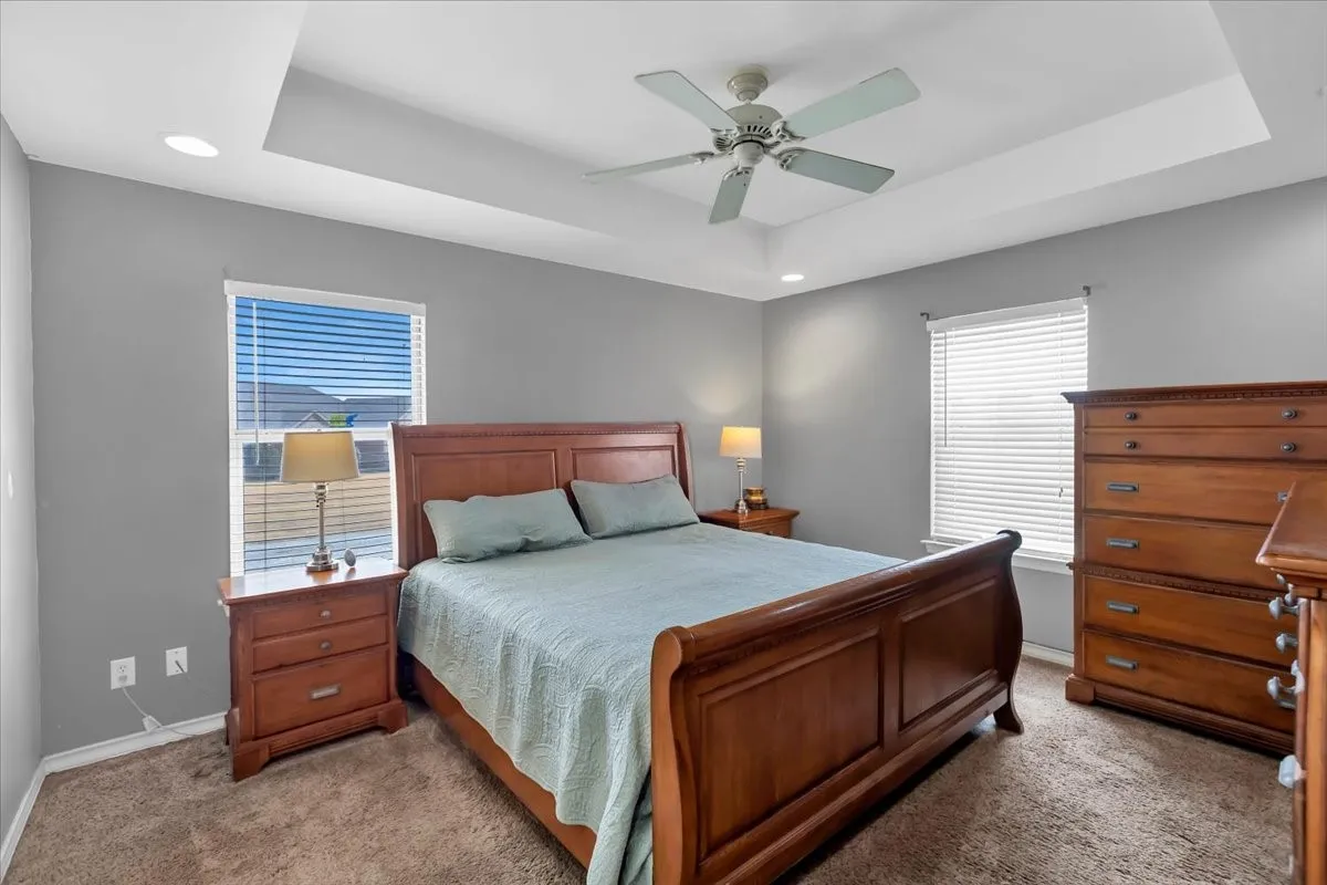 Tray ceiling, recessed lighting, ceiling fan, two windows with blinds, and carpeted flooring