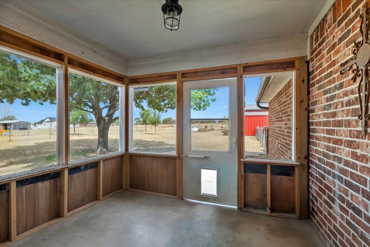 Screened porch featuring a concrete floor, exposed wood framing, and a brick exterior wall