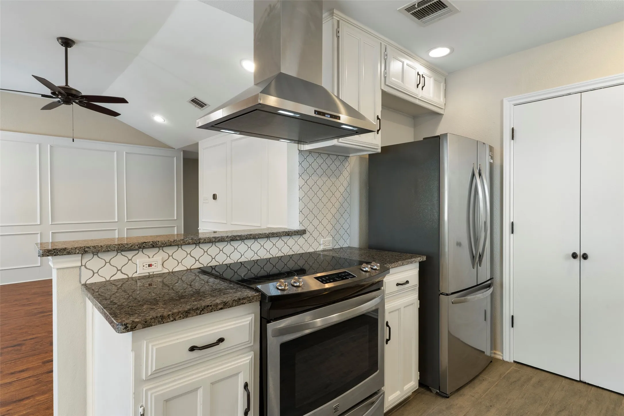 Kitchen featuring stainless steel appliances, granite countertops, white cabinetry, and an arabesque tile backsplash