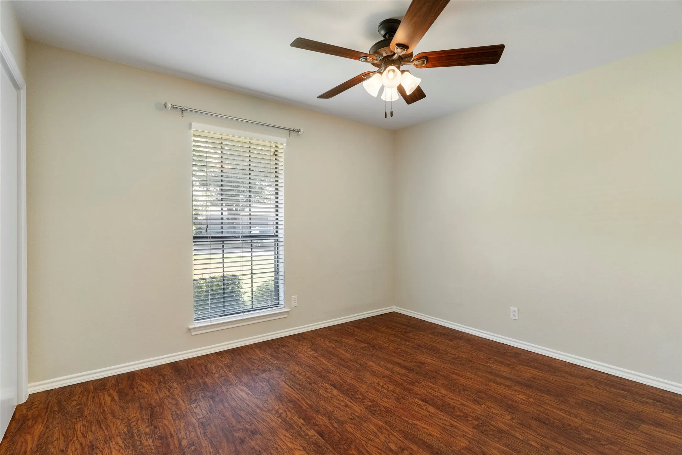 Wood-finish flooring, single window with blinds, ceiling fan with lighting, white trim, and neutral wall paint