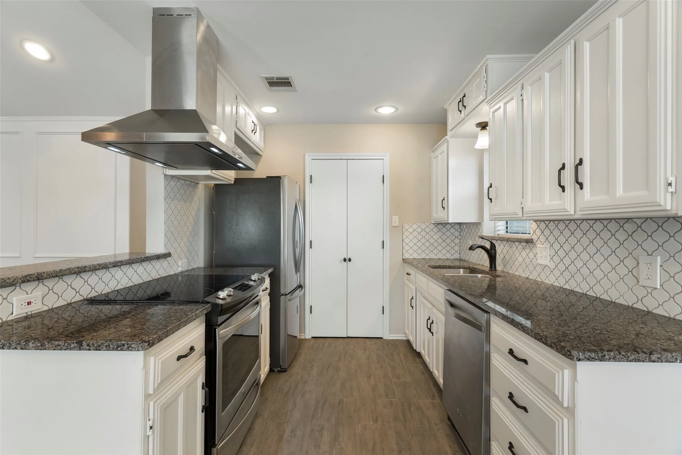 White cabinetry, stainless steel appliances, dark countertops, arabesque tile backsplash, and wood-finish flooring