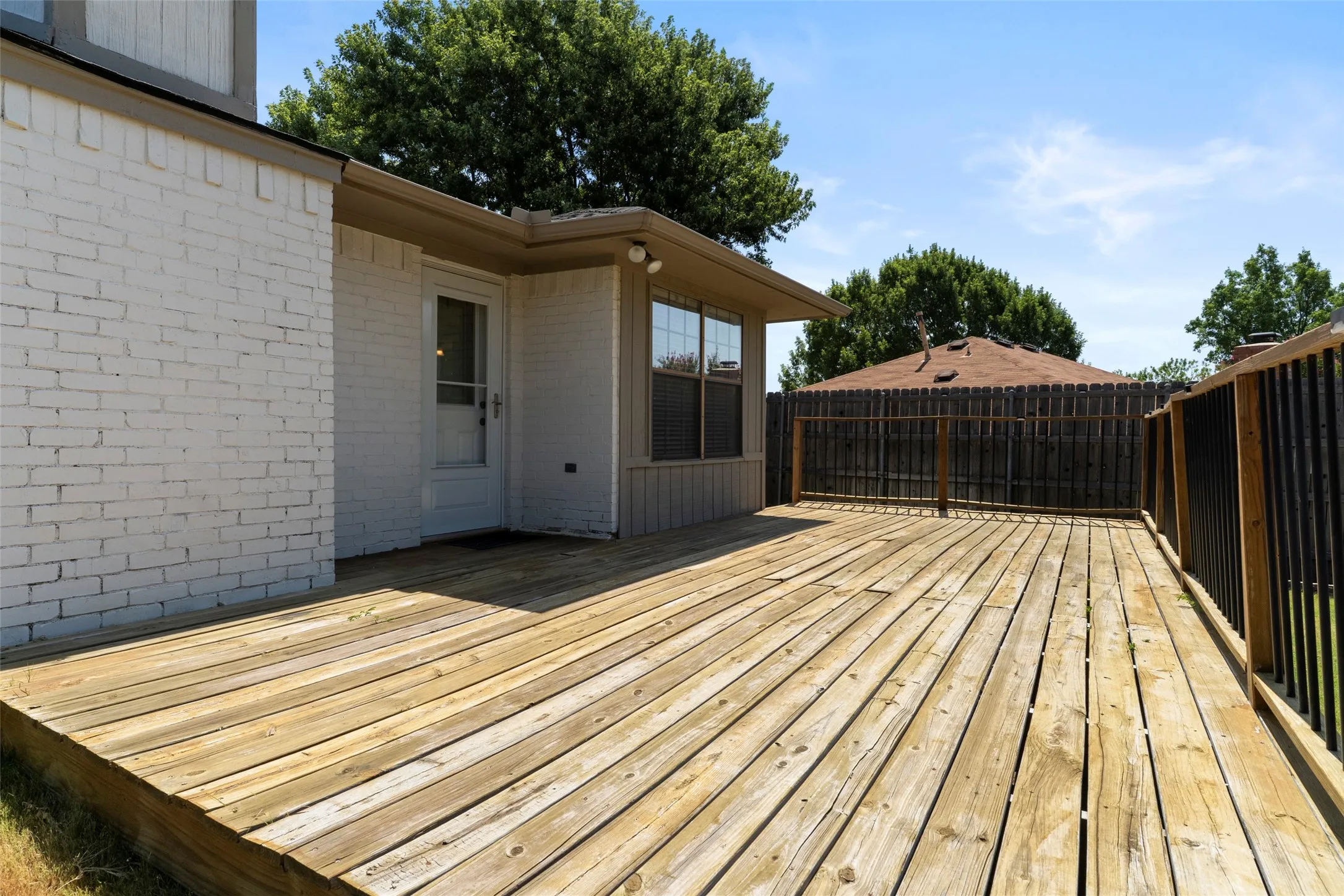 Expansive wood deck with a privacy fence, featuring a white brick exterior and exterior lighting