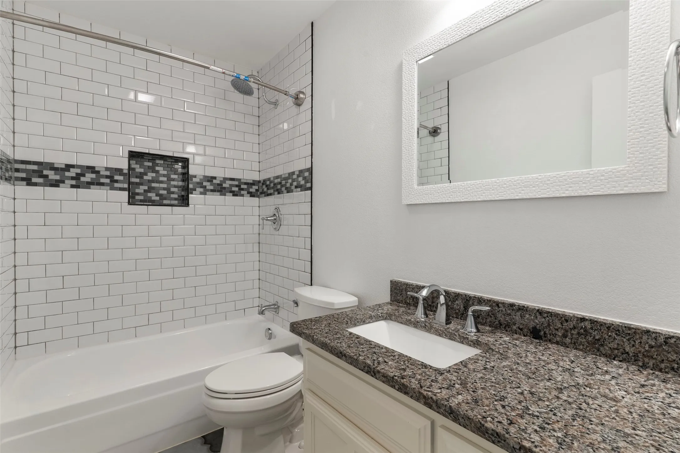 Subway tile shower surround with mosaic accent, built-in shower niche, chrome shower fixtures, white vanity with integrated sink, and speckled stone-finish countertop
