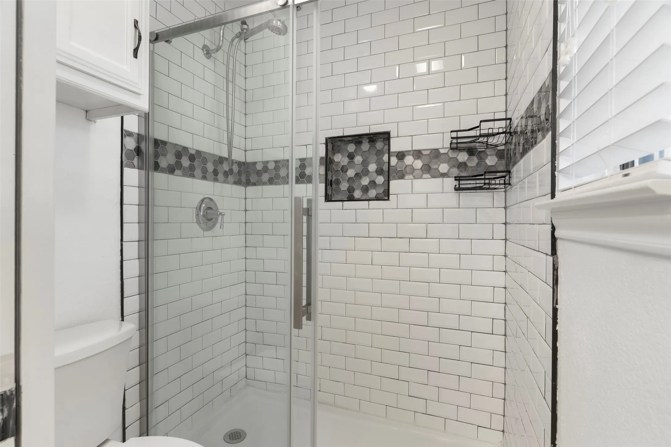 Enclosed shower featuring subway tile with a decorative hexagonal tile accent, a built-in shower niche, and a sliding glass door