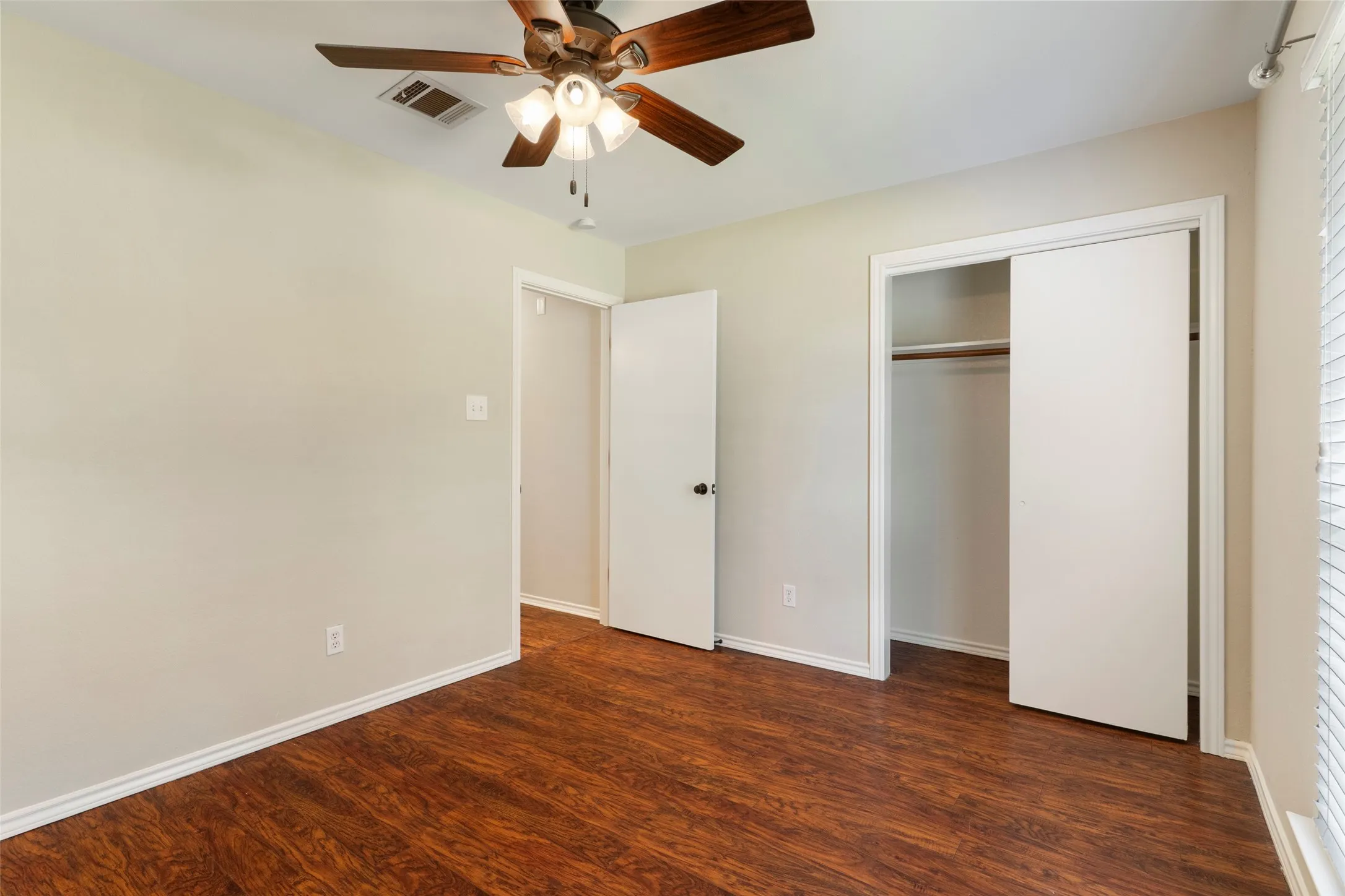Wood-finish flooring, ceiling fan with integrated lighting, window with horizontal blinds, and a built-in closet with sliding doors
