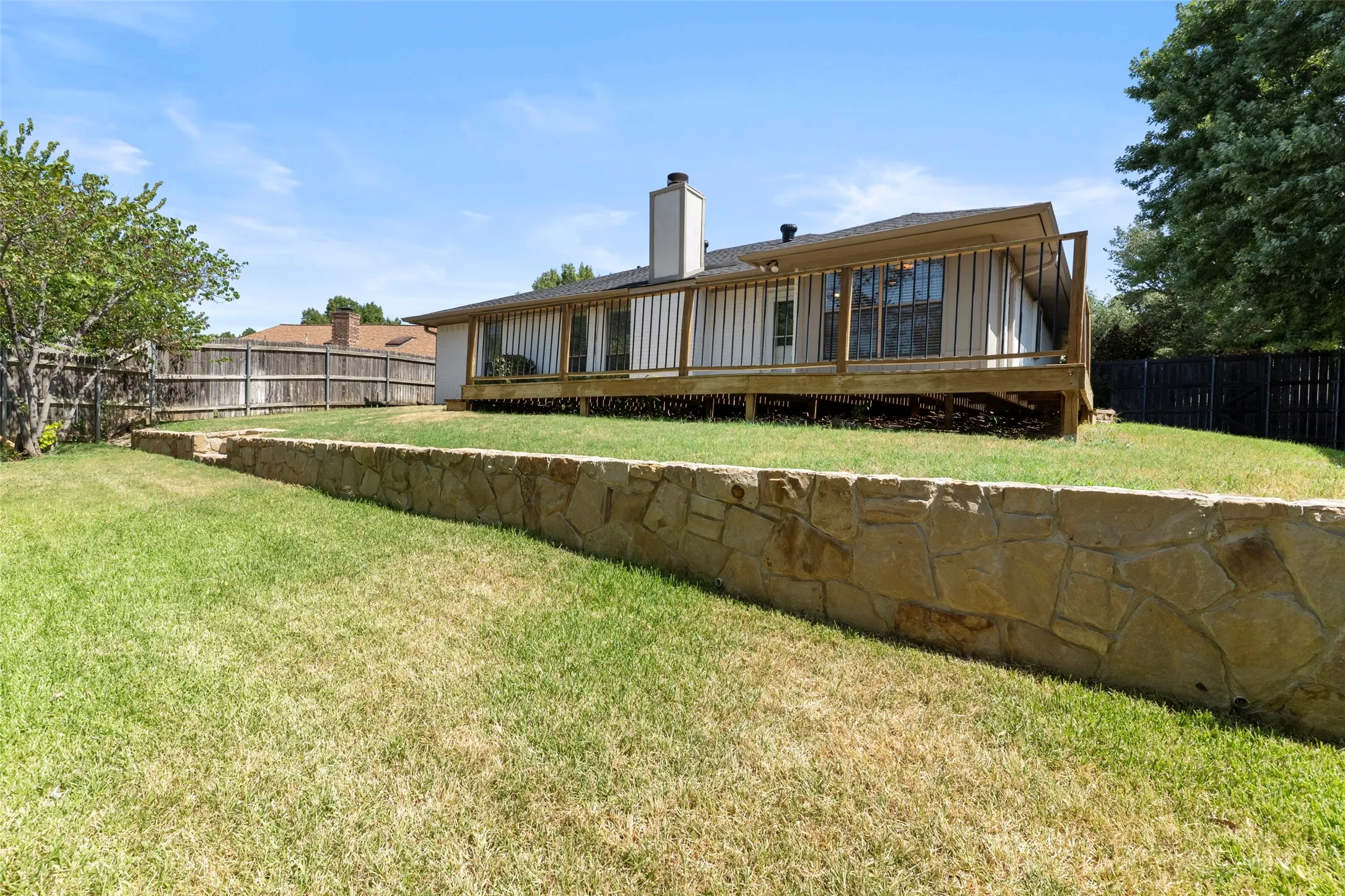 Expansive backyard with a stone retaining wall, tiered lawn, and a raised wood deck