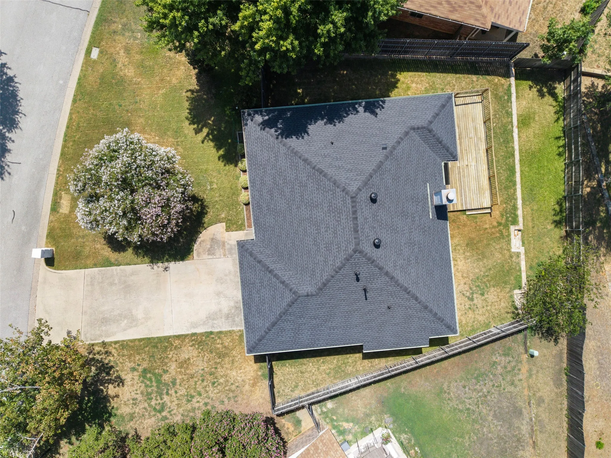 Gable roof with dark shingles, concrete driveway, front yard with mature trees, backyard with a wood deck, and a perimeter fence