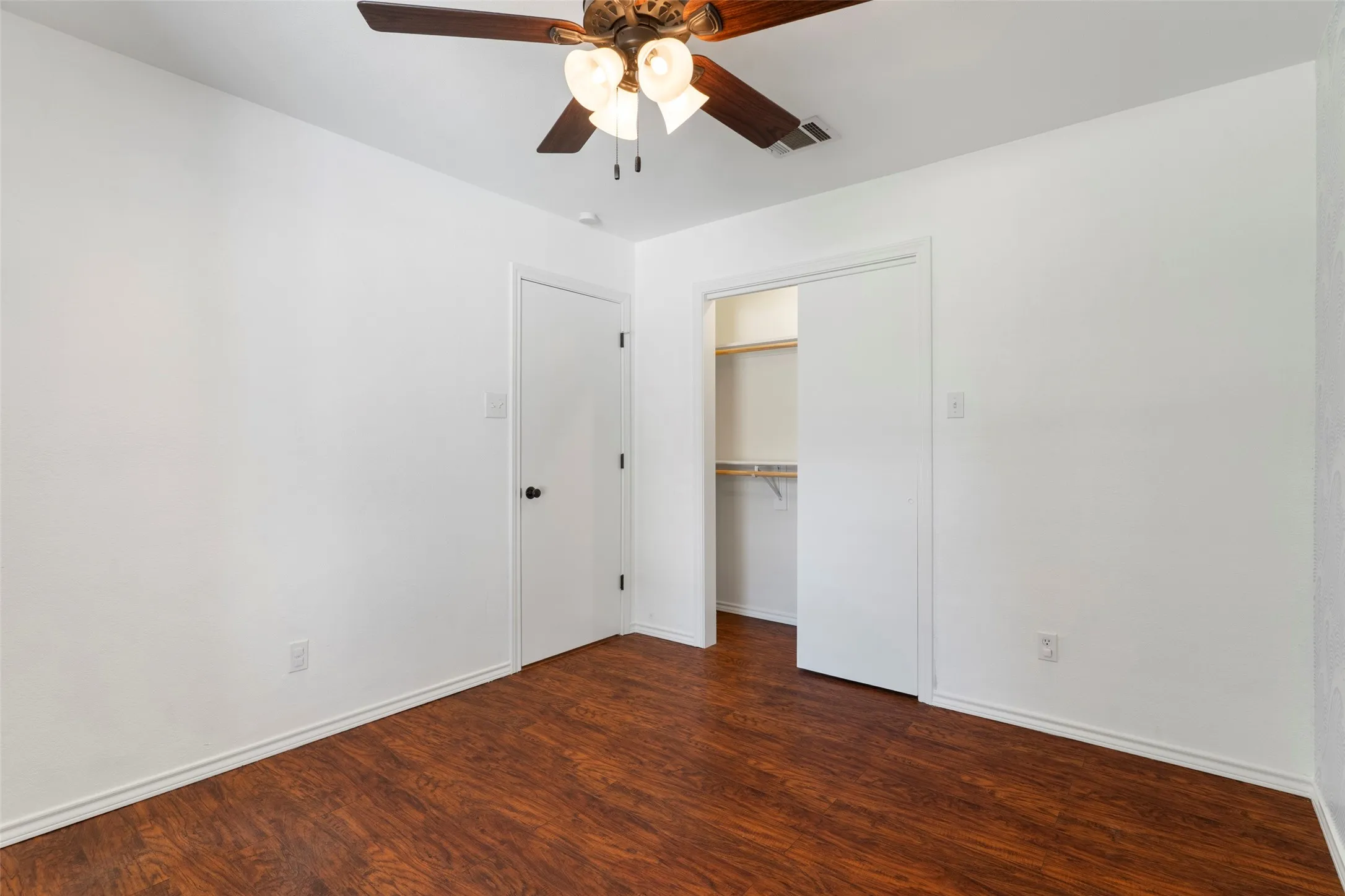 Wood-finish flooring, white walls, and a ceiling fan with integrated lighting