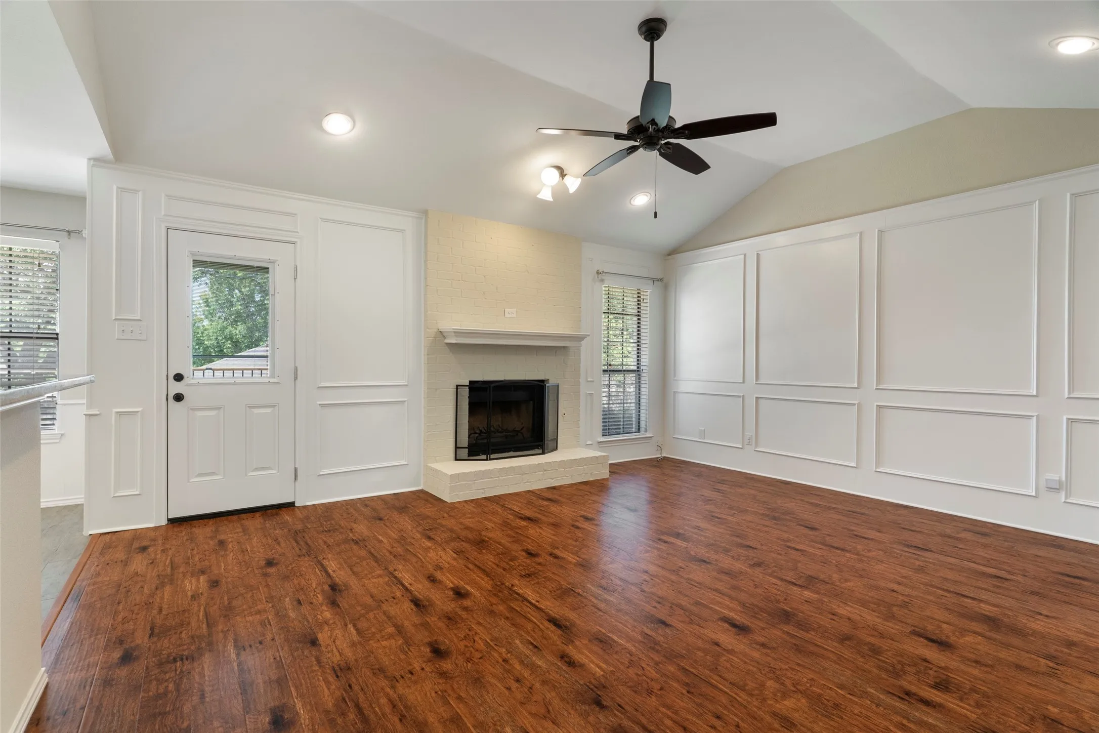 Vaulted ceiling, wood-finish flooring, built-in fireplace, ceiling fan, and decorative wall molding