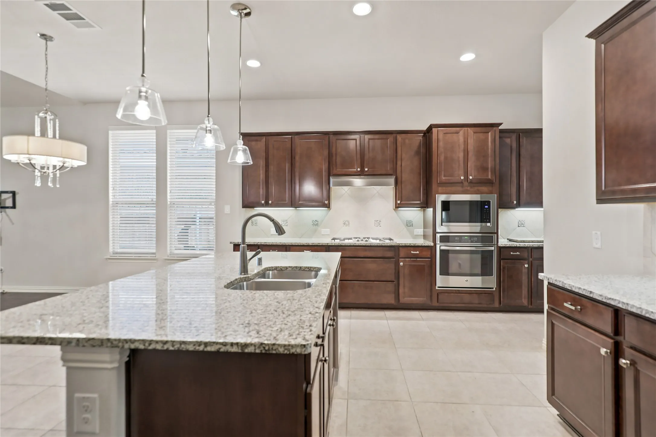 Spacious kitchen featuring an expansive island with a double basin sink, dark wood cabinetry, integrated stainless steel appliances, and tile flooring