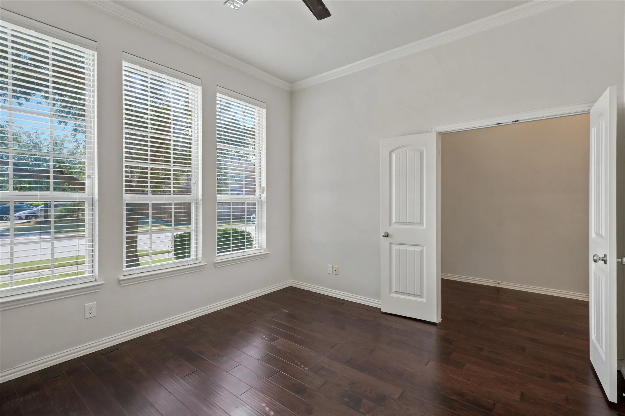 Dark wood-finish flooring, three large windows with blinds, crown molding, and a white paneled door