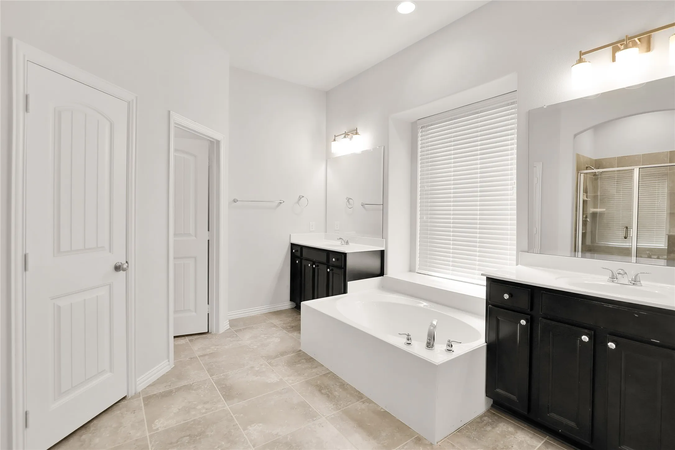 Dual vanity sinks, built-in soaking tub, tiled flooring, dark wood-finish cabinetry, and a walk-in shower with tiled surround