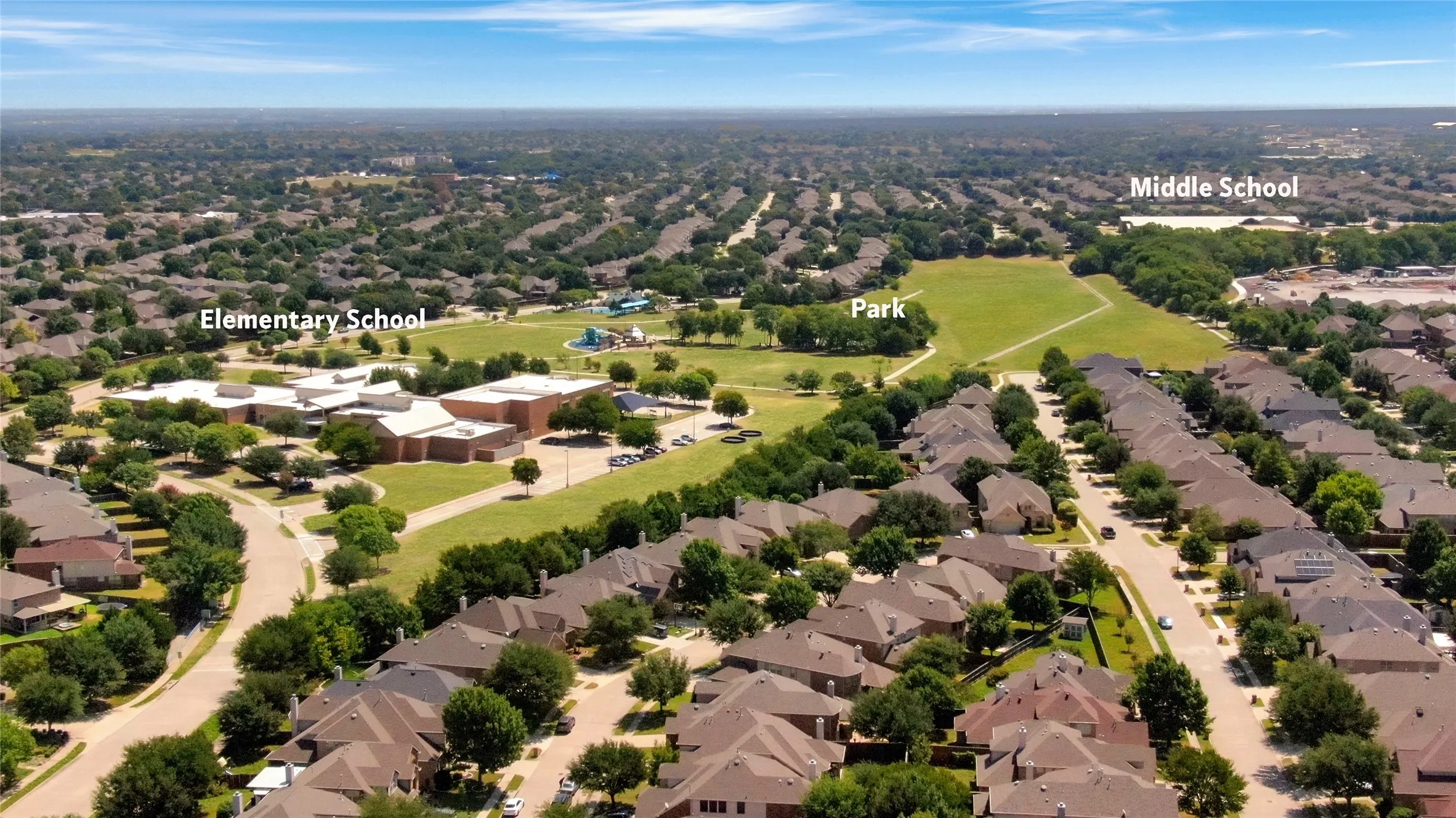 Residential neighborhood with tree-lined streets, a large green space, and visible school buildings