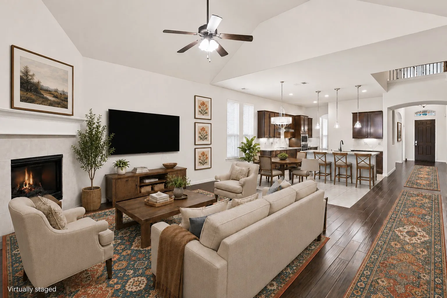 Open-concept living space featuring a wood-burning fireplace with stone surround, wall-mounted flat-screen television, wood-finish flooring throughout, and ceiling fan with integrated lighting
