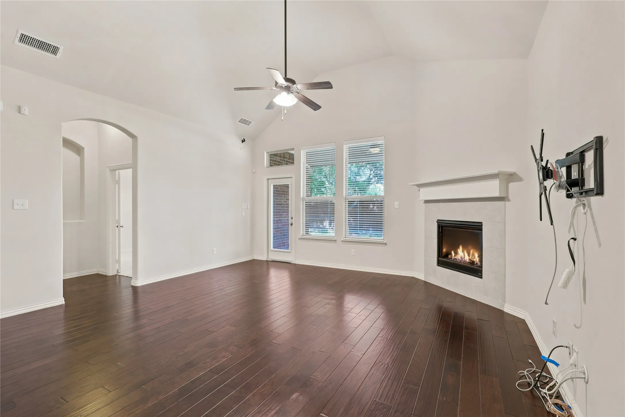 Vaulted ceiling with a ceiling fan, dark wood-finish flooring, and a fireplace with a white mantel