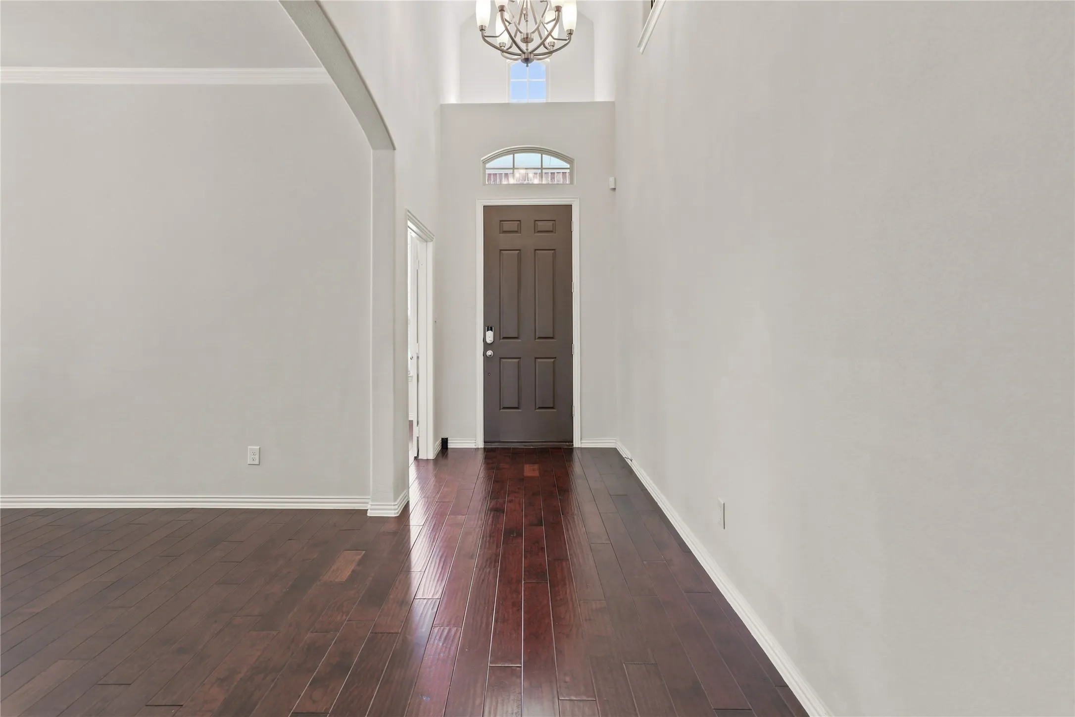 Two-story entryway featuring a dark wood-finish door with an arched transom window, a decorative chandelier, and dark wood-finish flooring