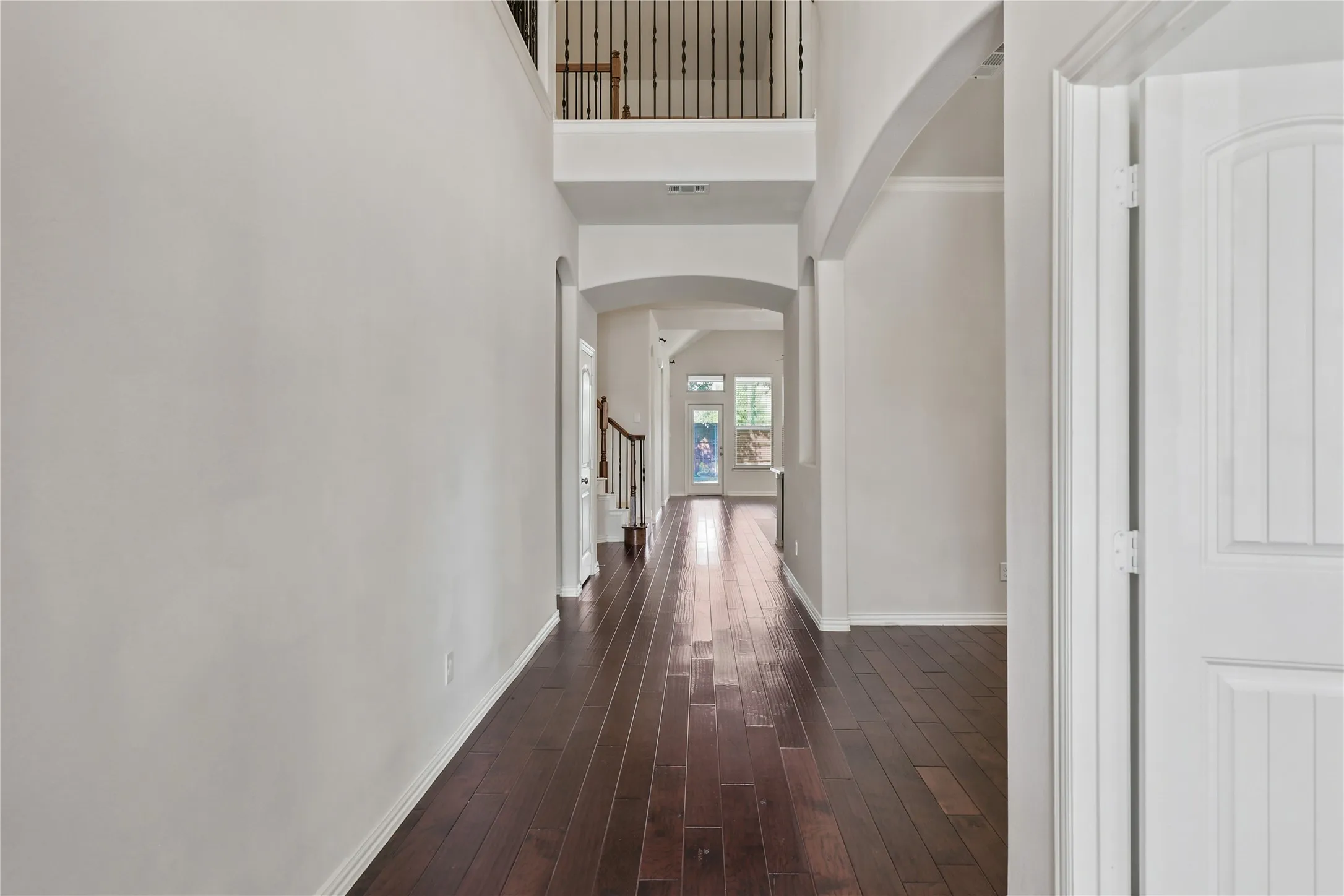 Two-story foyer featuring dark wood-finish flooring, a wrought iron banister, and arched doorways