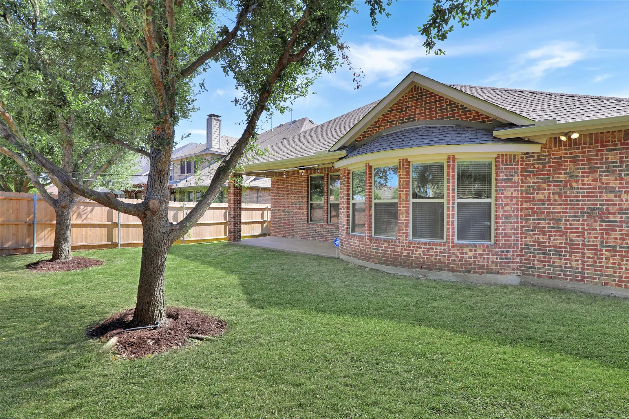 Spacious backyard featuring a manicured lawn, established trees, and a privacy fence