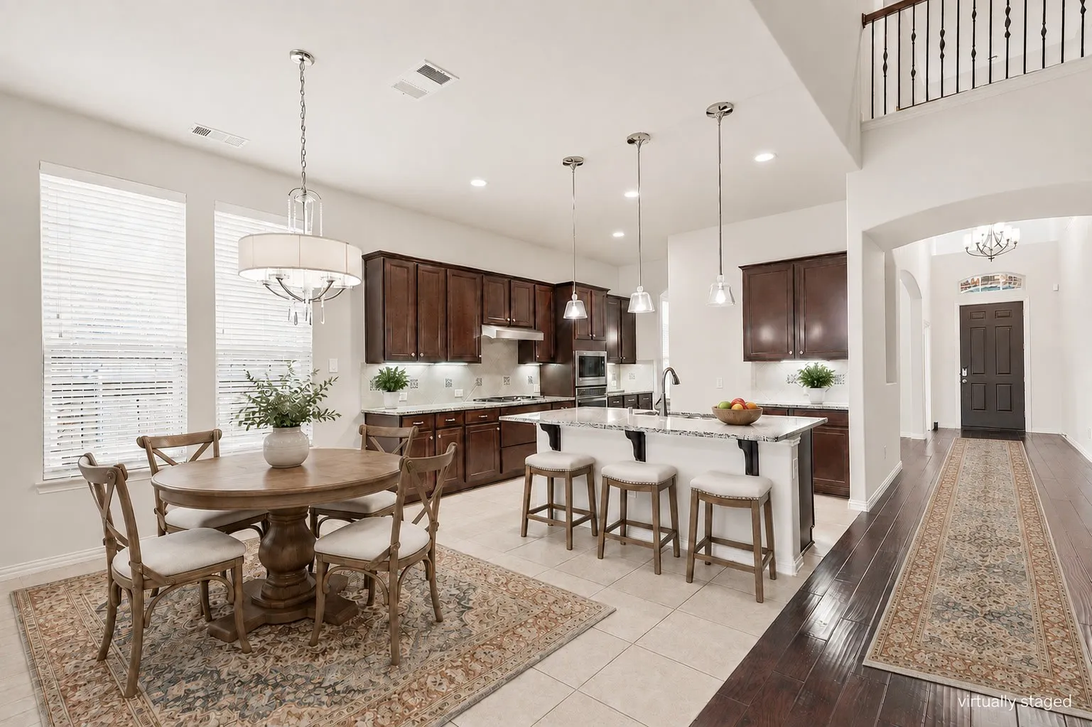 Open-concept kitchen and dining area featuring dark wood cabinetry with stainless steel appliances, white quartz countertops, pendant lighting over a center island with seating, and a round dining table