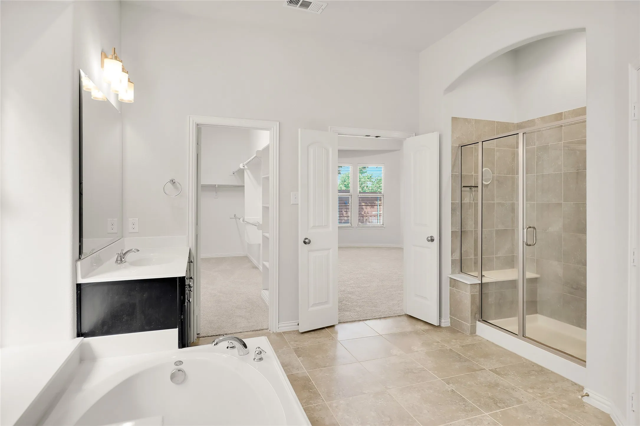 Tiled flooring with a white soaking tub, a dark wood-finish vanity with a single sink, a tiled walk-in shower with a glass enclosure and bench, and vaulted ceilings