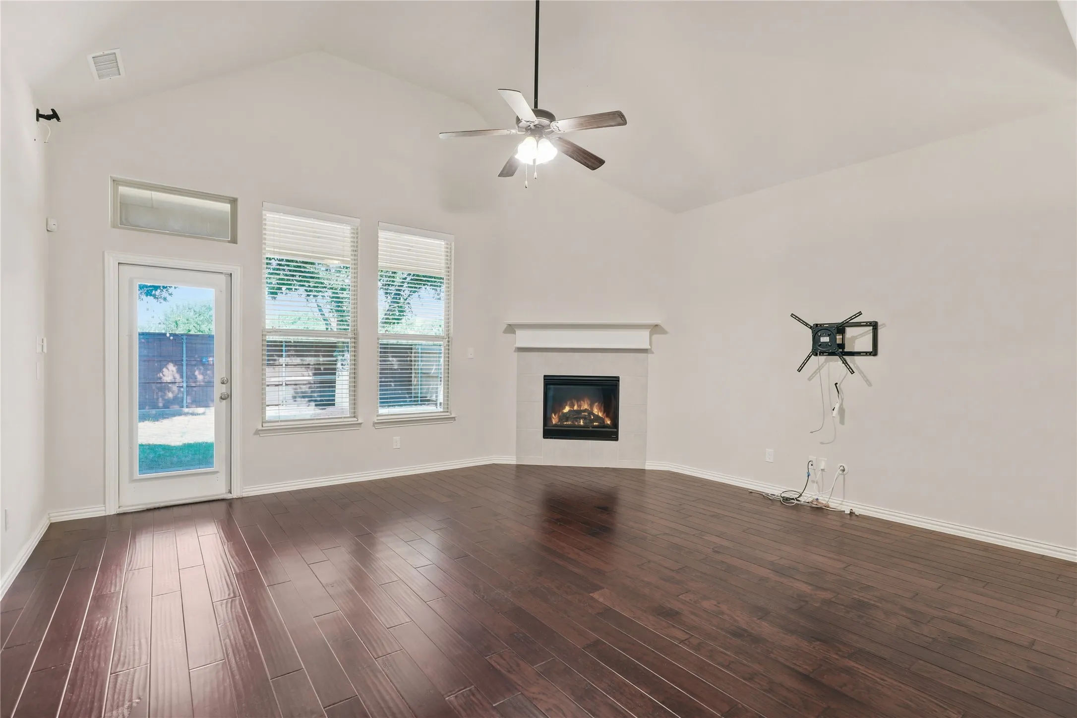 Vaulted ceiling with a ceiling fan, gas fireplace with a mantel, dark wood-finish flooring, and multiple windows with blinds