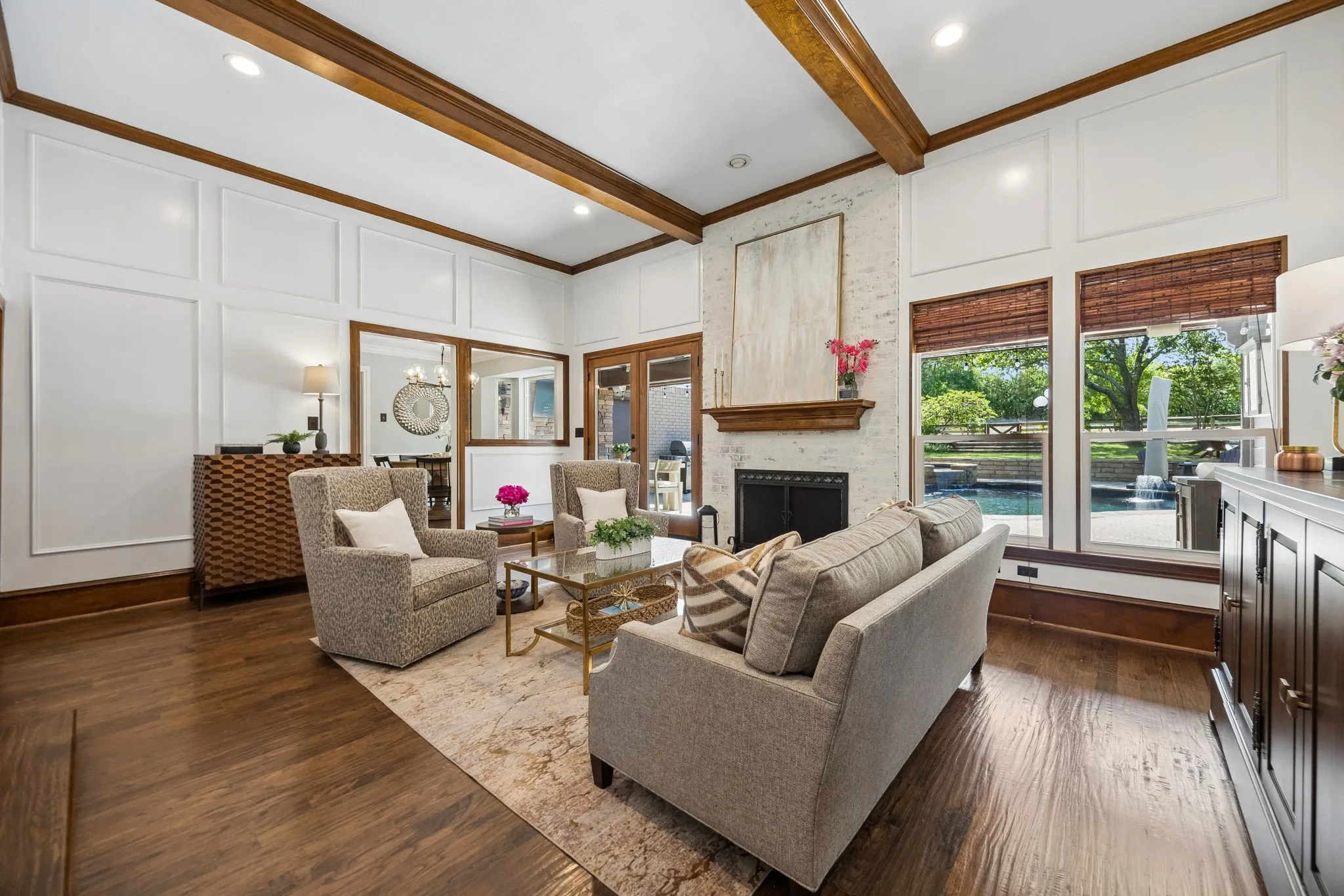 Living room with exposed ceiling beams, brick fireplace with large windows with views of the pool.