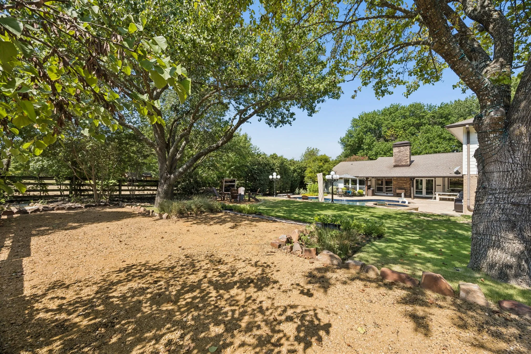 Peaceful backyard featuring established trees, a stone patio, and an in-ground swimming pool