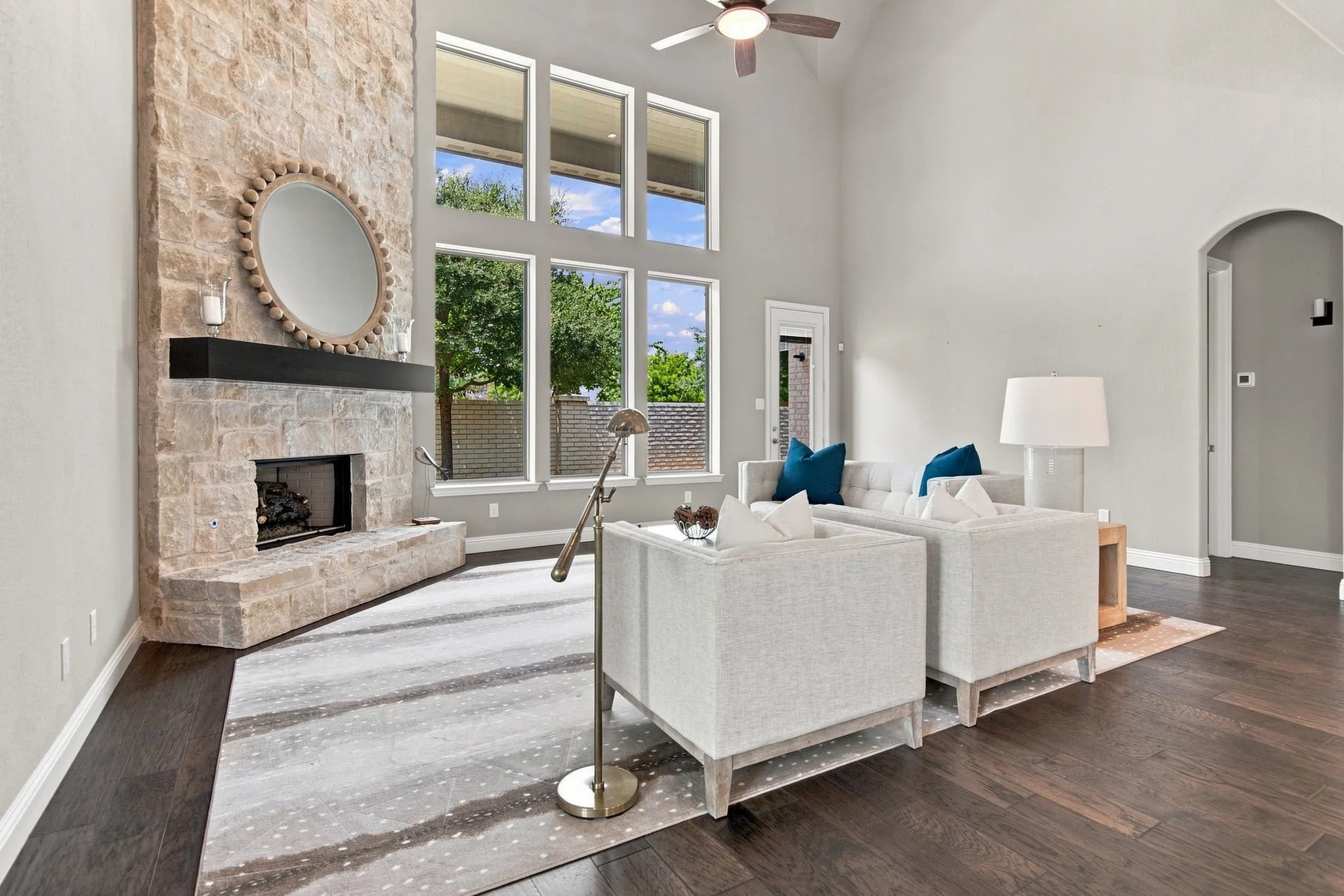 Vaulted ceiling with a ceiling fan, a full-height stone-clad fireplace with a black wood mantel, and expansive windows