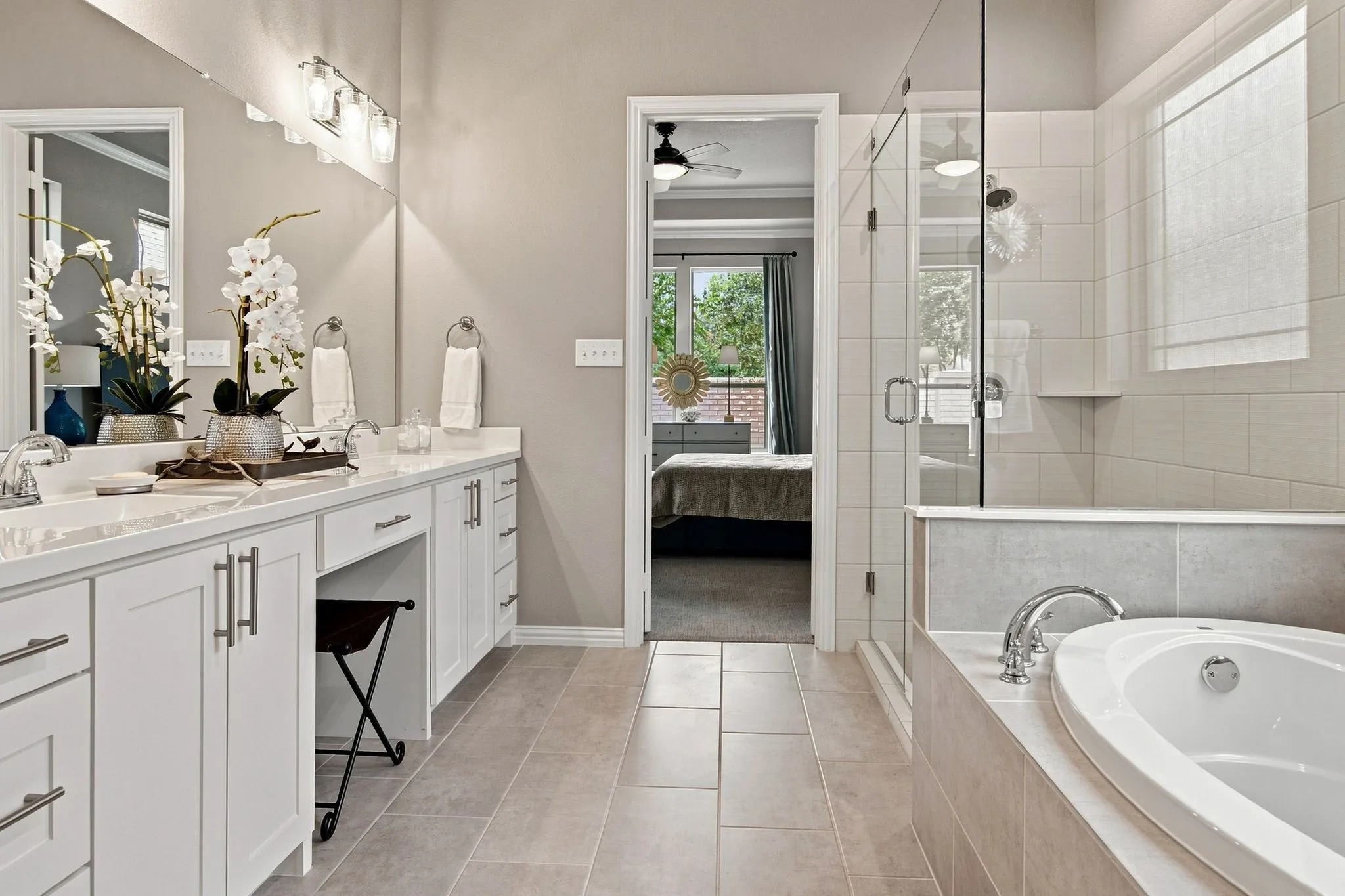 Dual vanity with white cabinetry and chrome hardware, a built-in makeup counter, a glass-enclosed shower, and a built-in soaking tub