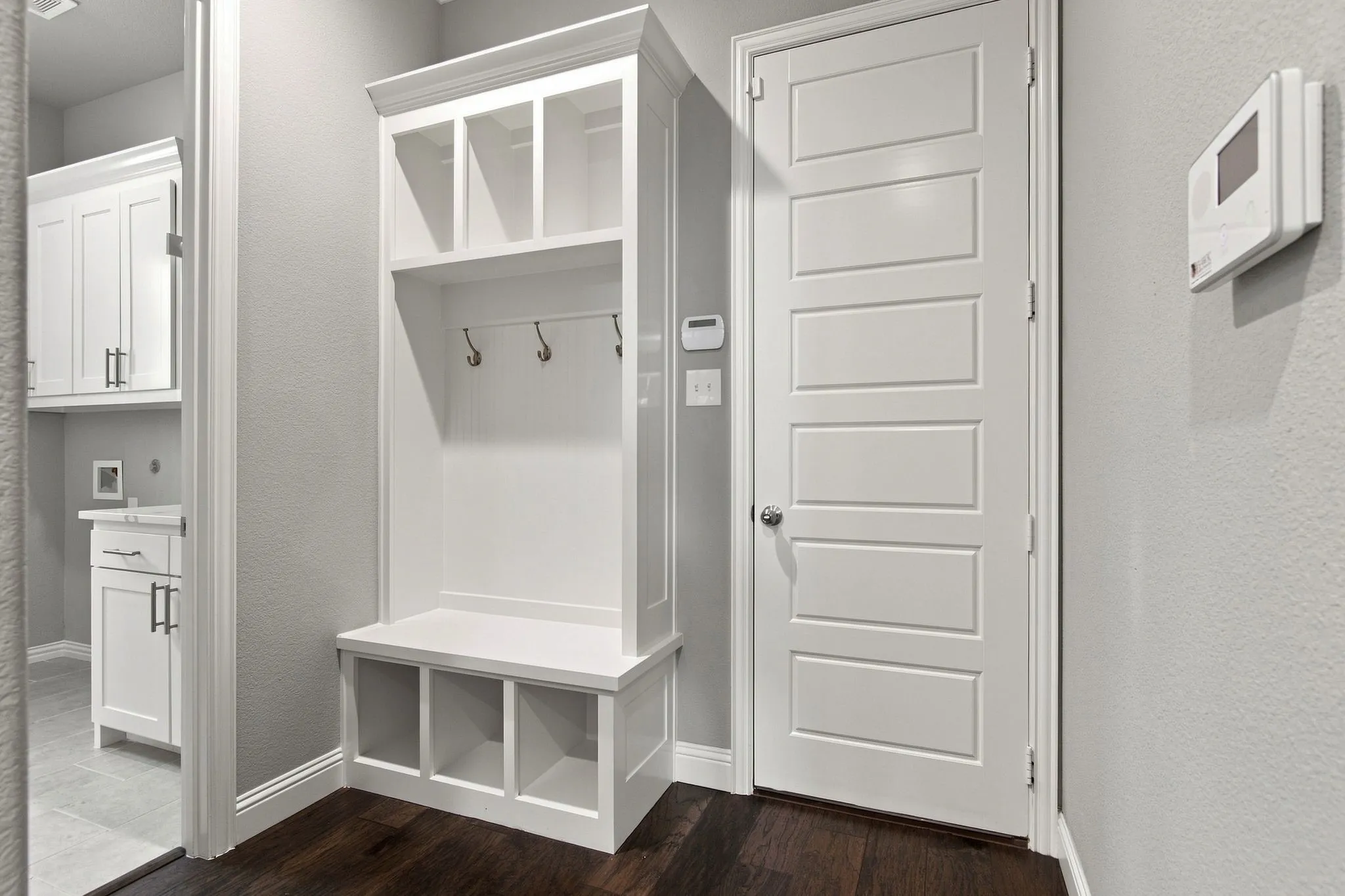 Built-in mudroom bench with cubbies and coat hooks, dark wood-finish flooring, and a five-panel interior door