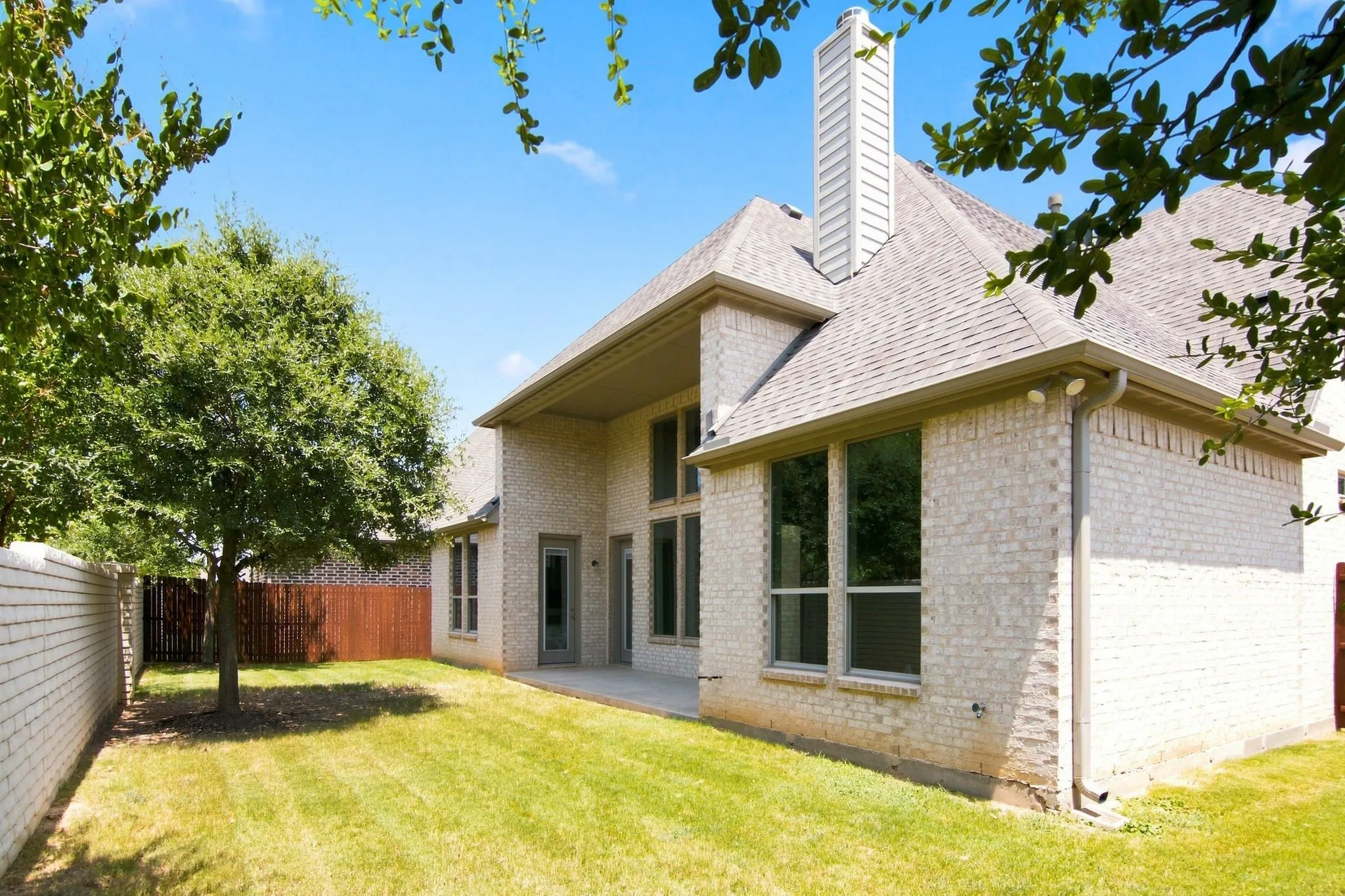 Expansive backyard with a manicured lawn, full brick exterior, and a concrete patio