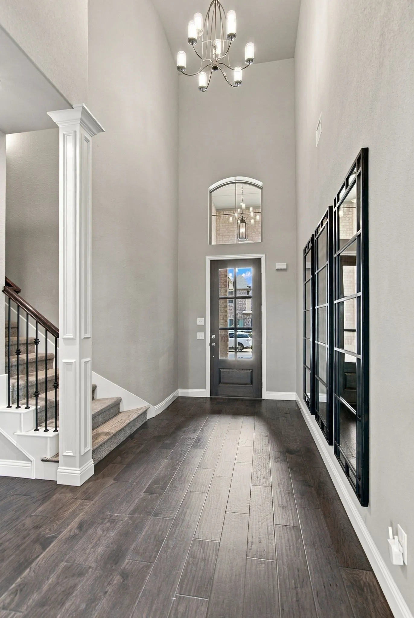 Two-story foyer featuring an arched window, a contemporary chandelier, a dark wood-finish flooring, and a staircase with wrought iron balusters