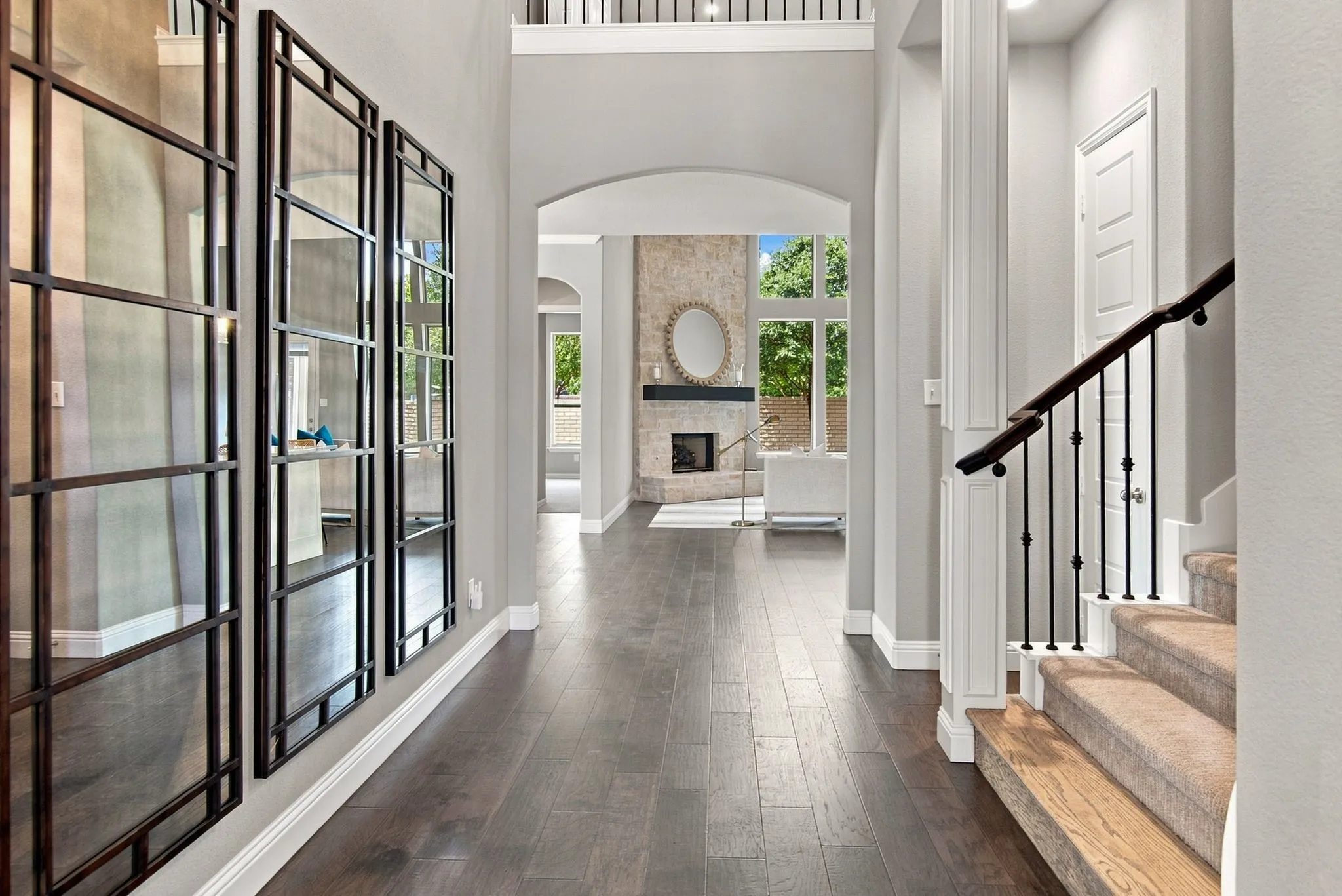 Hardwood-finish flooring, staircase with carpeted treads and wrought iron balusters, stone-faced fireplace, arched doorways, and high ceilings