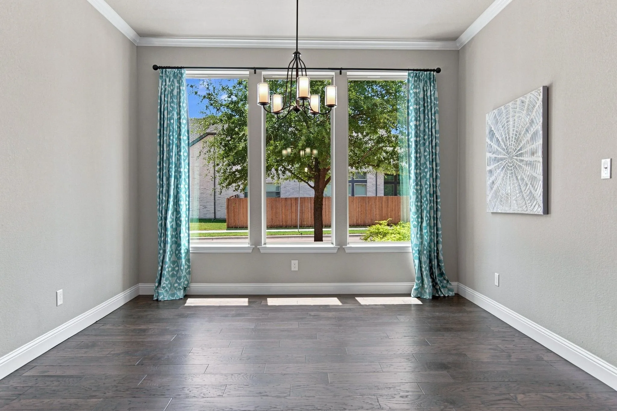 Expansive window arrangement, dark wood-finish flooring, overhead chandelier, crown molding, and substantial baseboards