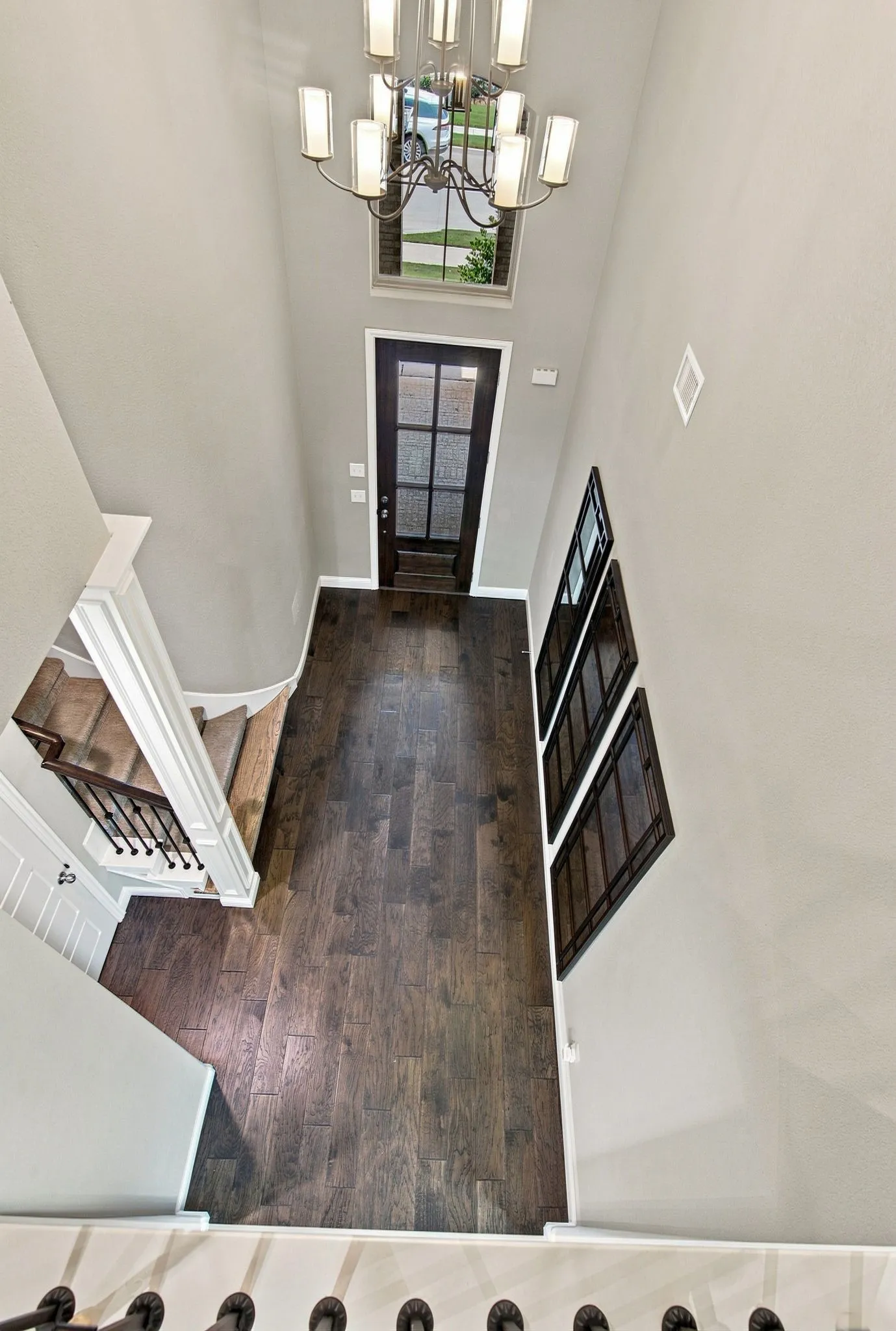 Two-story foyer with dark wood-finish flooring, a contemporary chandelier, and a transom window above the entry door