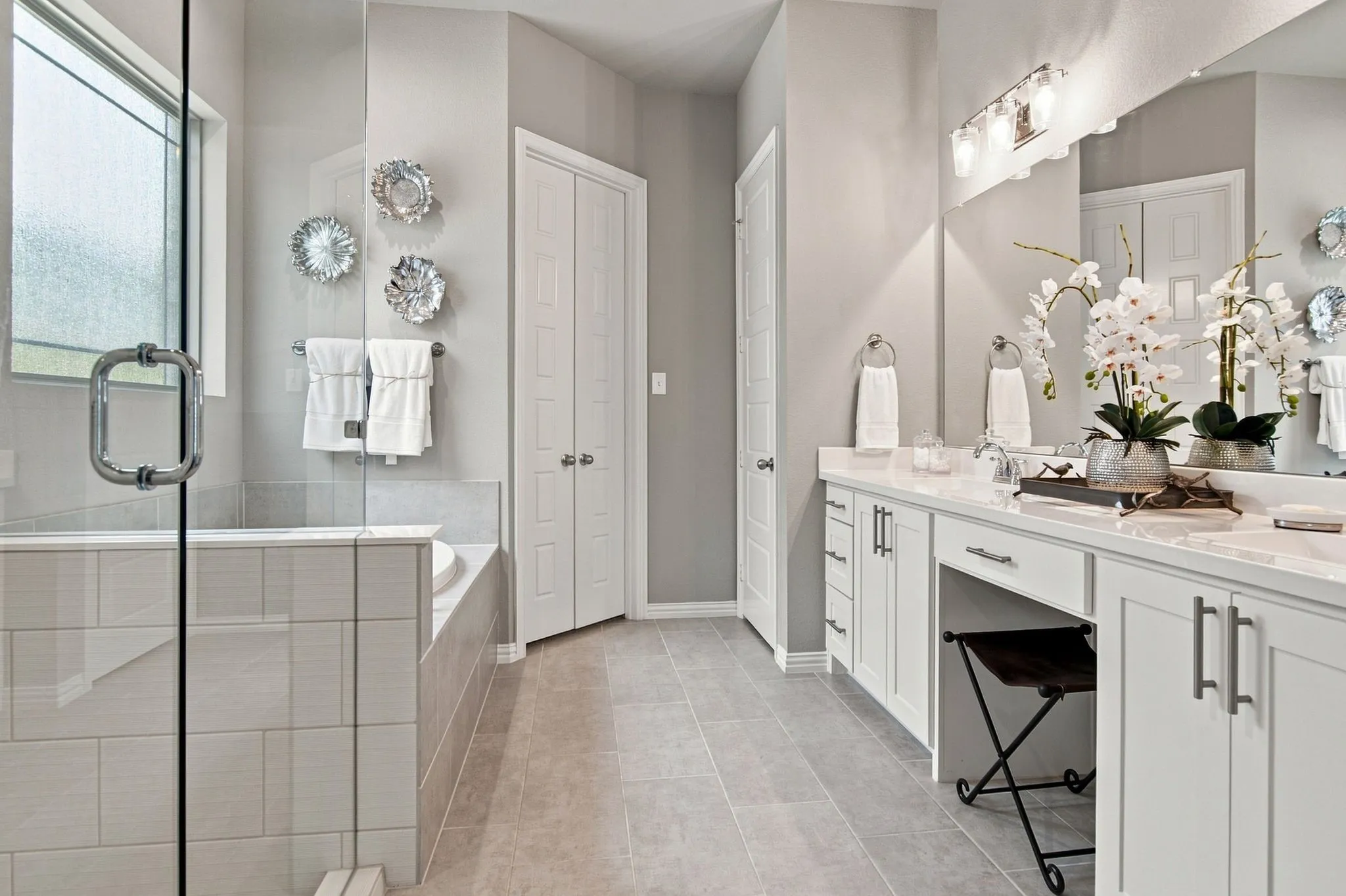 Spacious bathroom with a glass-enclosed shower, built-in soaking tub, extensive vanity with dual sinks, makeup desk, and tile flooring