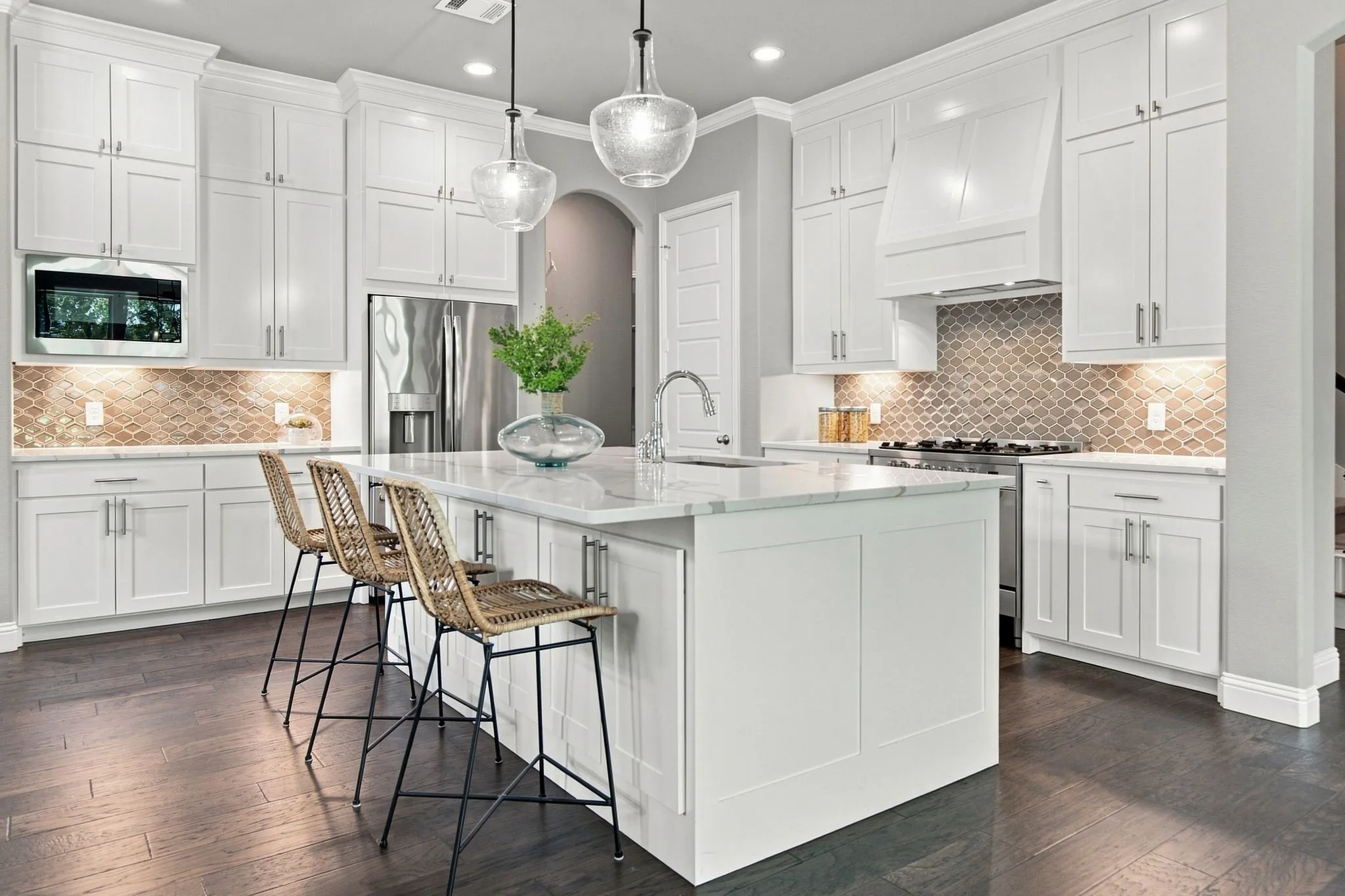 White shaker-style cabinetry with crown molding, a central island with a stone countertop, a decorative backsplash, stainless steel appliances, and wood-finish flooring