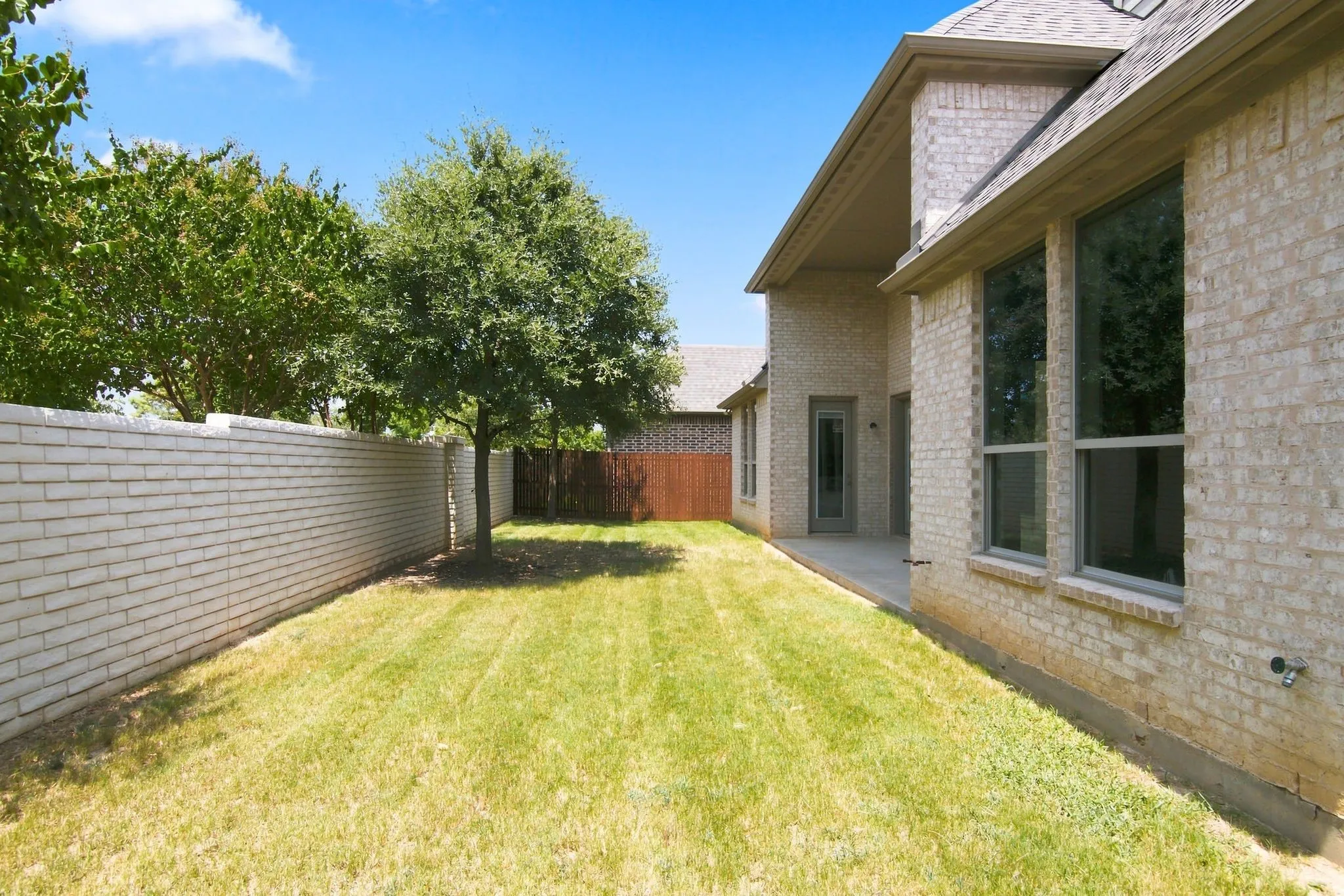 Expansive lawn area with a mature tree, bordered by a substantial white brick privacy wall