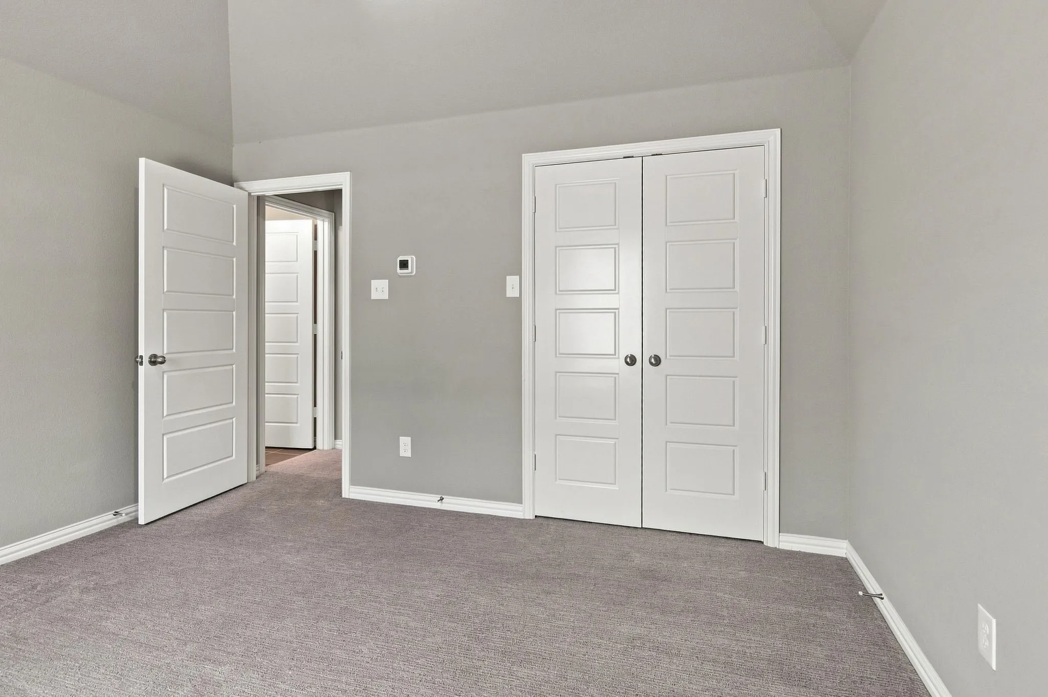 Neutral gray wall paint, gray carpeting, white five-panel interior doors, and white bi-fold closet doors