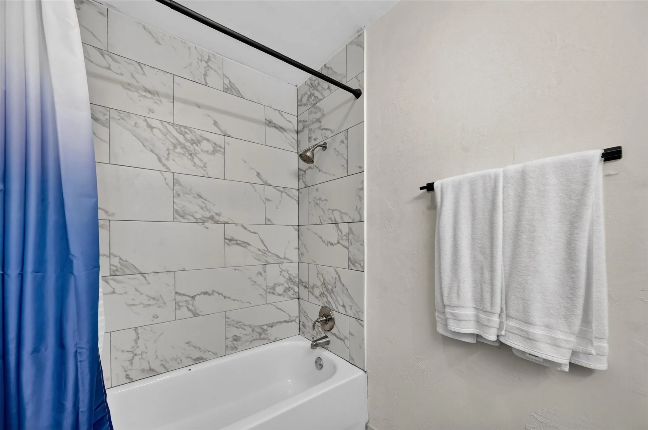 Bathtub with integrated shower, subway-style wall tiling, and a wall-mounted showerhead