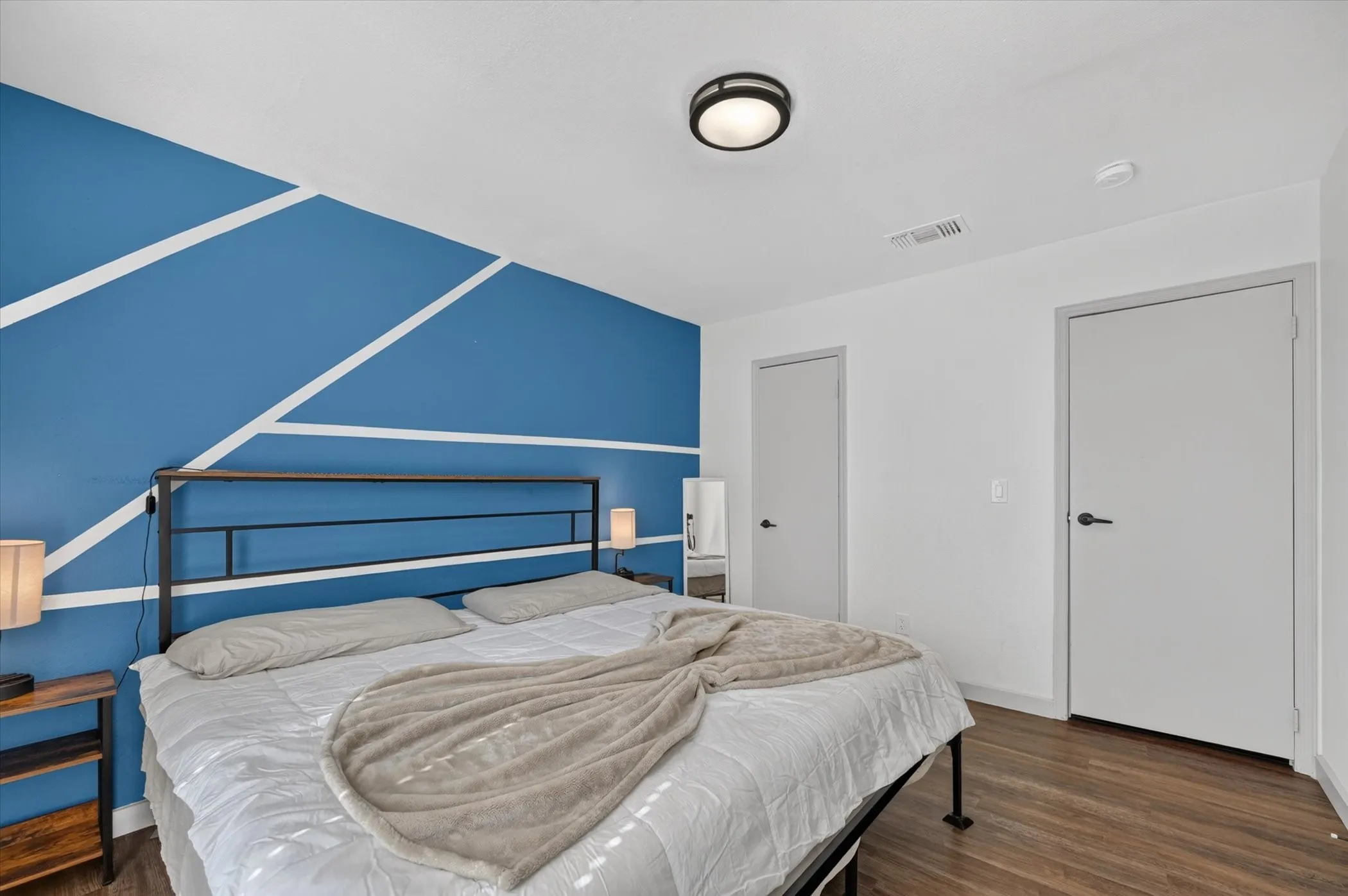 Accent wall featuring a geometric paint design, ceiling-mounted light fixture, and wood-finish flooring