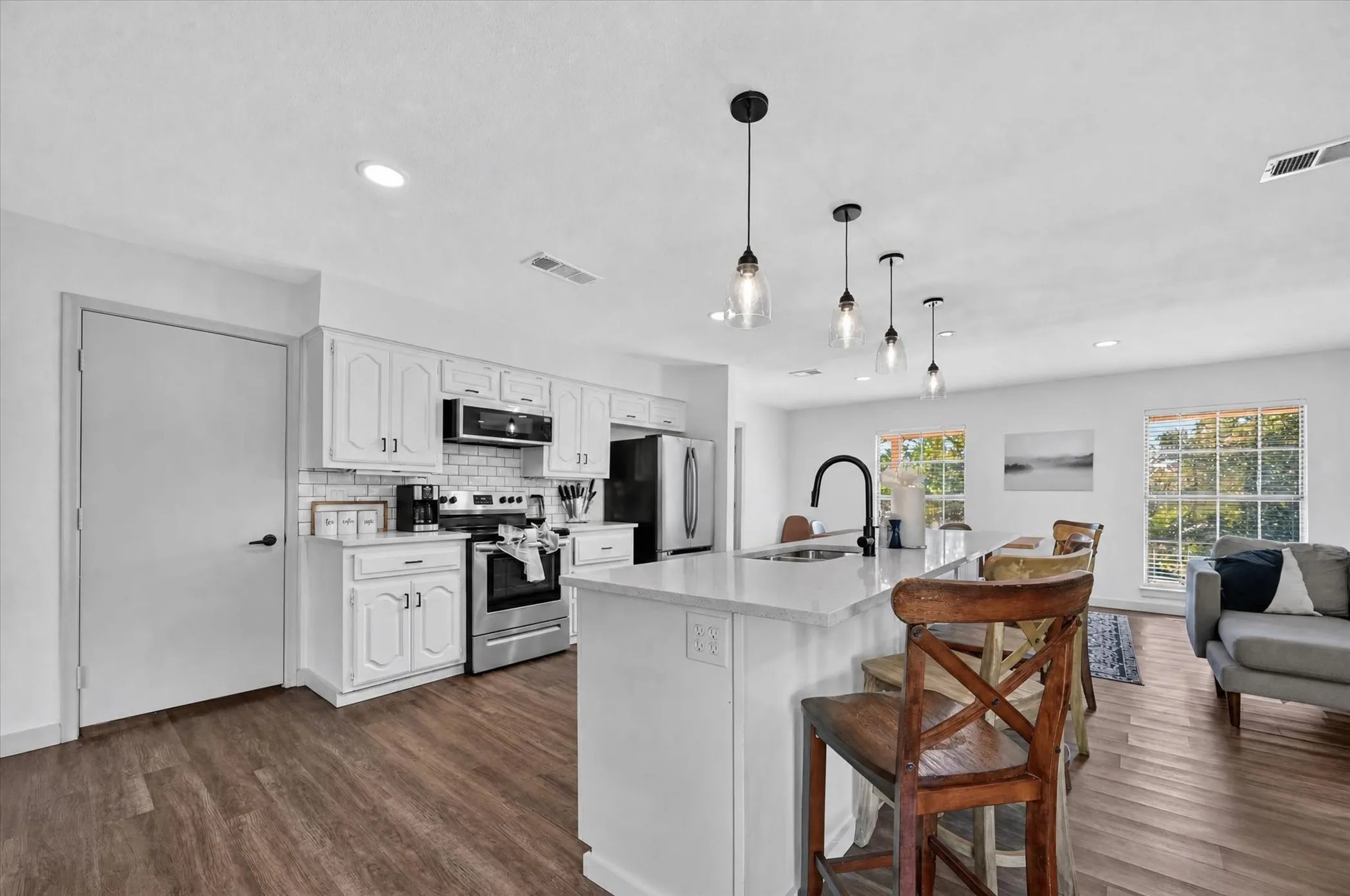 Kitchen featuring white cabinetry, subway tile backsplash, stainless steel appliances, and an island with a sink and breakfast bar