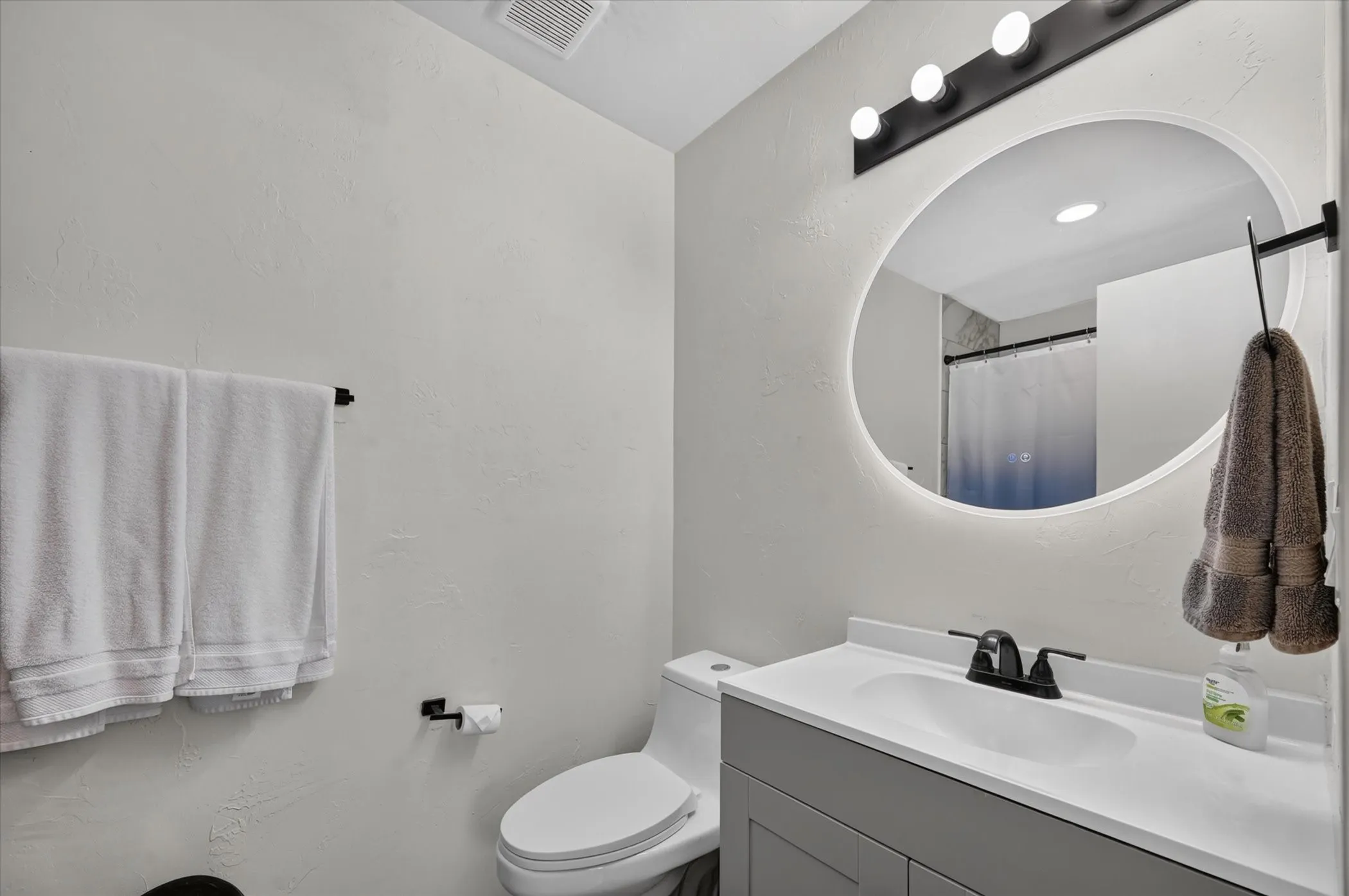 Modern vanity with a white countertop and integrated sink, illuminated oval mirror, and matte black fixtures