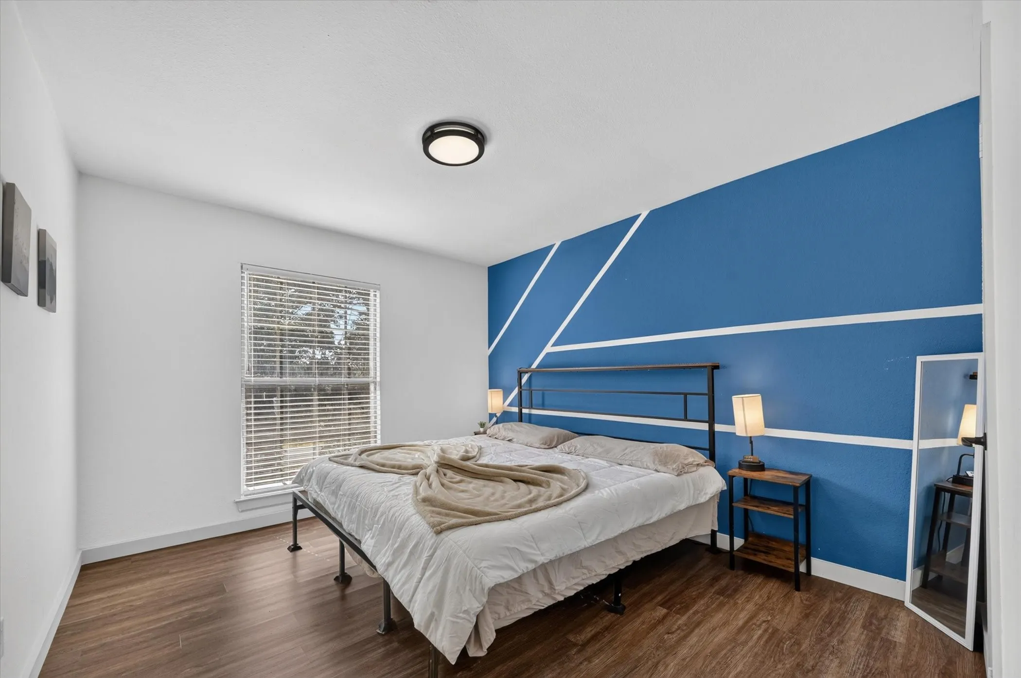Wood-finish flooring, accent wall with geometric molding, flush mount ceiling light, and window with blinds