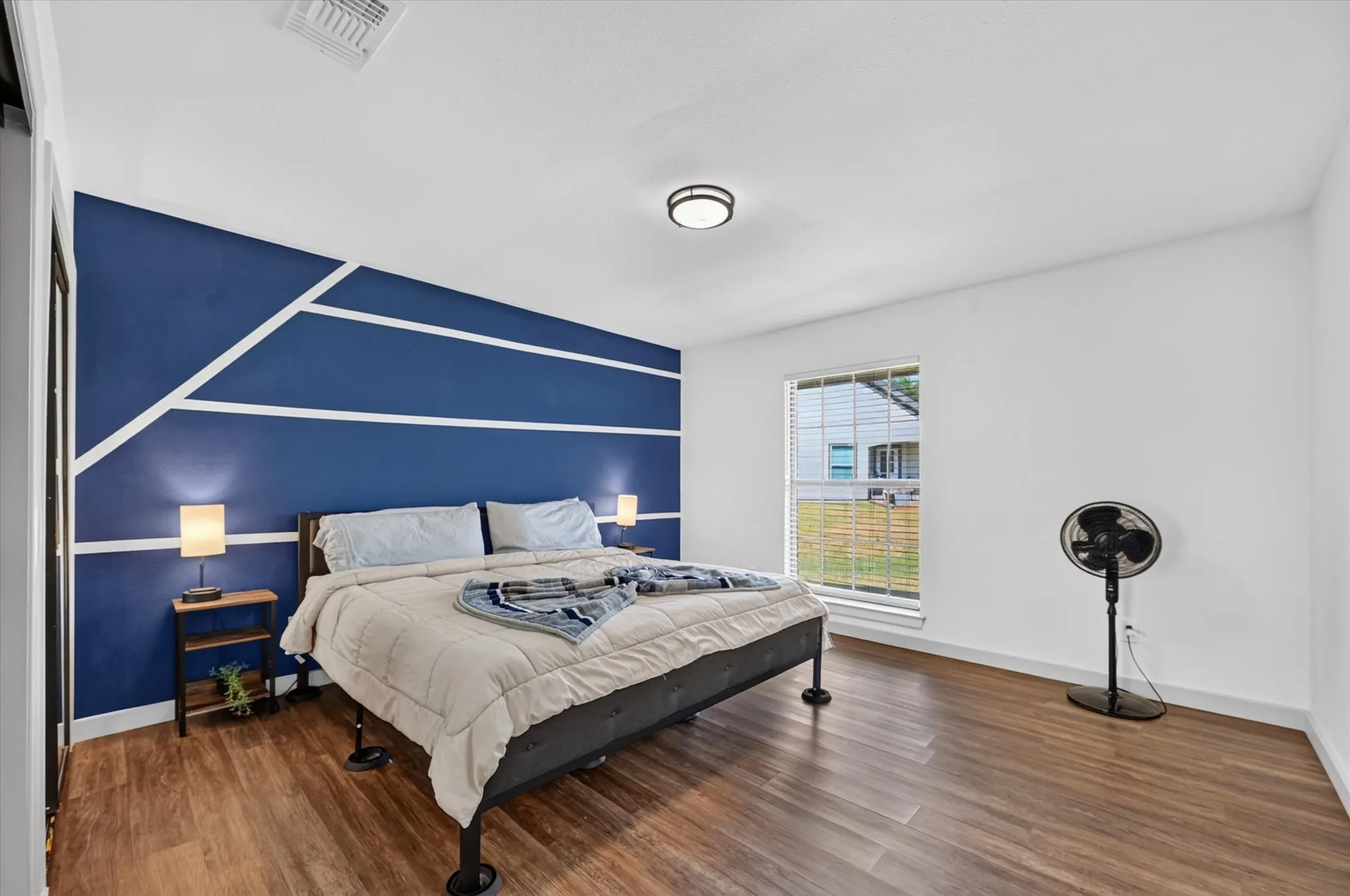 Wood-finish flooring, a painted accent wall with geometric trim, and a window with blinds