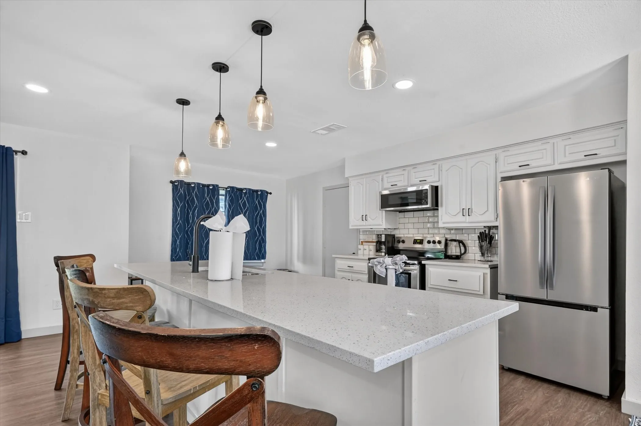 Kitchen featuring white cabinetry, subway tile backsplash, stainless steel appliances, a center island with a light-toned countertop, and clear glass pendant lighting