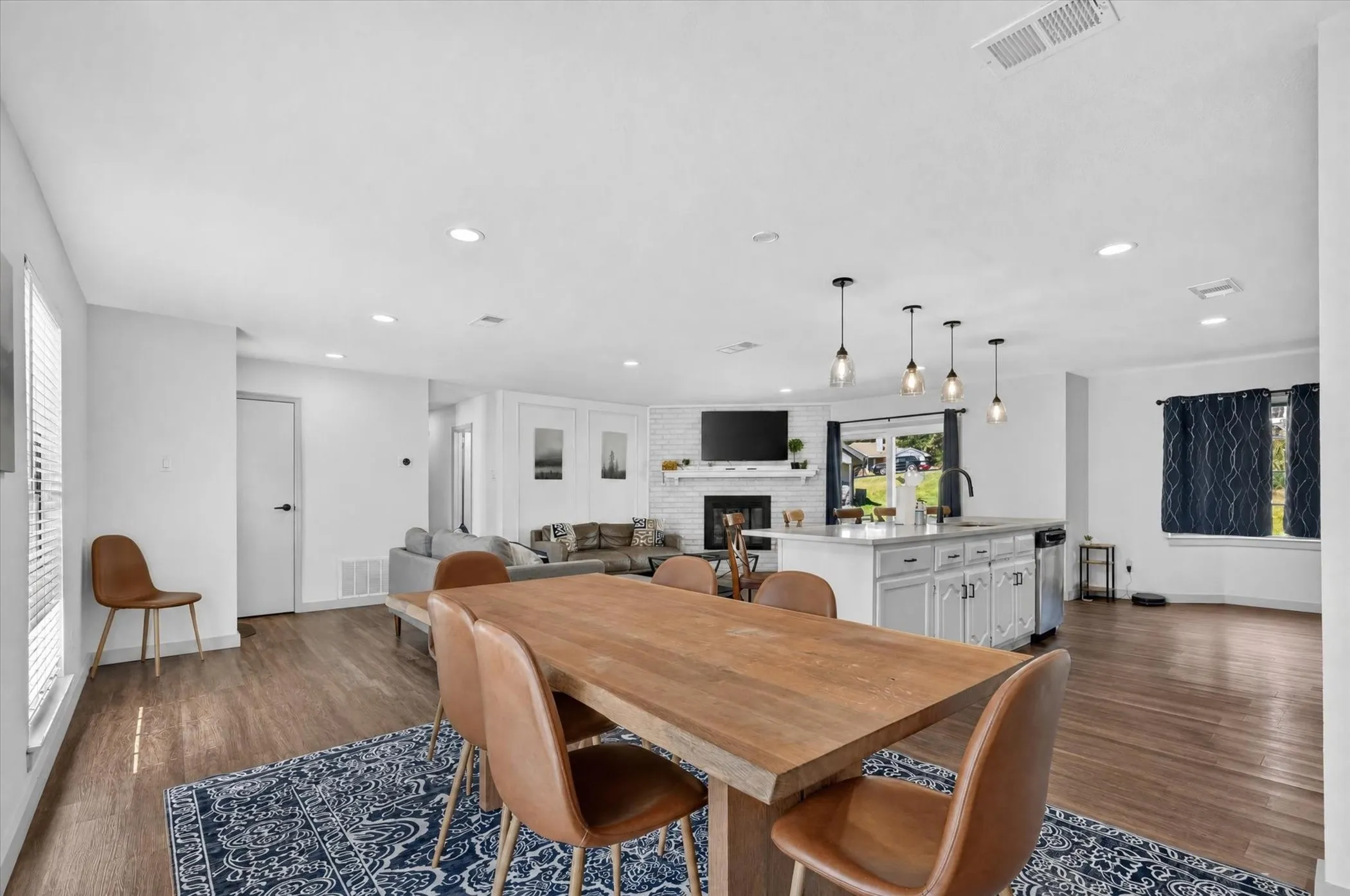 Wood-finish flooring throughout, recessed ceiling lighting, kitchen island with built-in cabinetry, pendant lighting, and a white brick fireplace